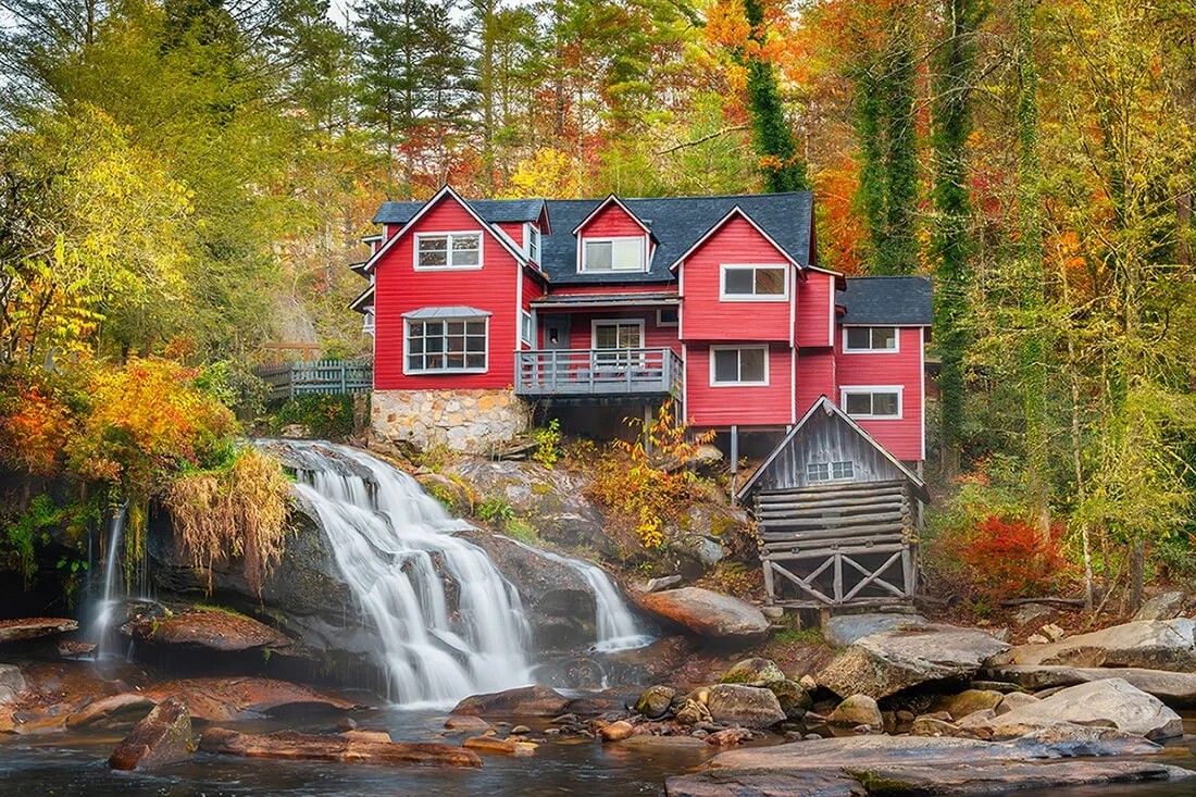 Red old mill house at Mill Shoals Falls on the French Broad River, surrounded by vibrant fall colors in the Blue Ridge Mountains of North Carolina. Landscape photography highlighting historic architecture, autumn foliage, and scenic river views. Idea