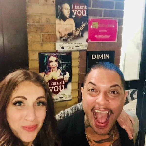 Emily and Raymond in a selfie in front of a poster for their show I Haunt You in New York City