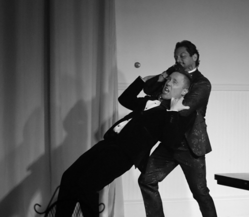 Two actors in tuxedos engage in stage combat with one holding the other in a headlock in Robbie, an immersive theater show in Eureka Springs Arkansas, near Fayetteville, Bentonville, Rogers, and Springdale.