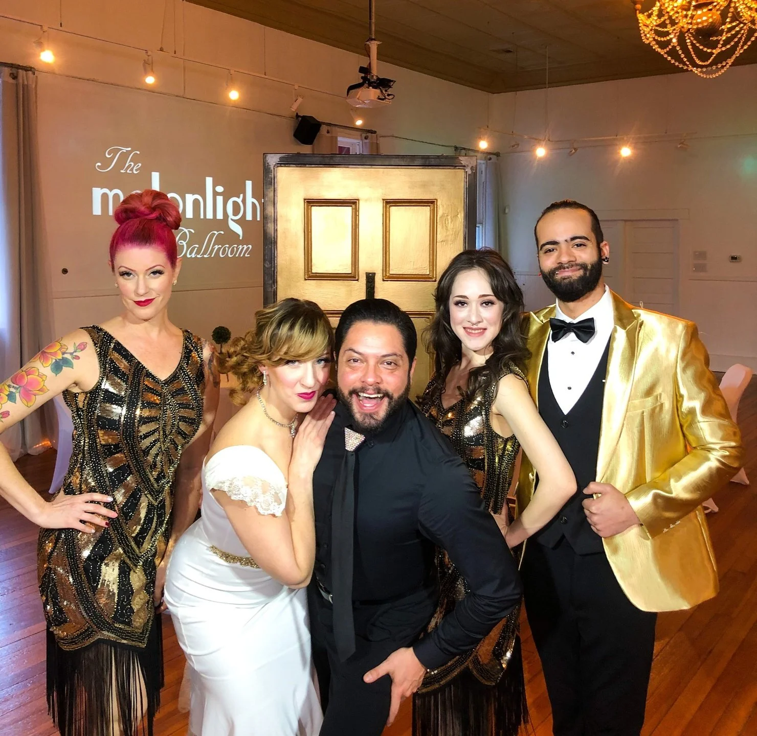 Emily and Raymond pose with their professional ensemble for a venue tour of the Melonlight Ballroom. Emily is wearing a white wedding dress, Raymond in all black, and the rest don 1920's inspired costumes.