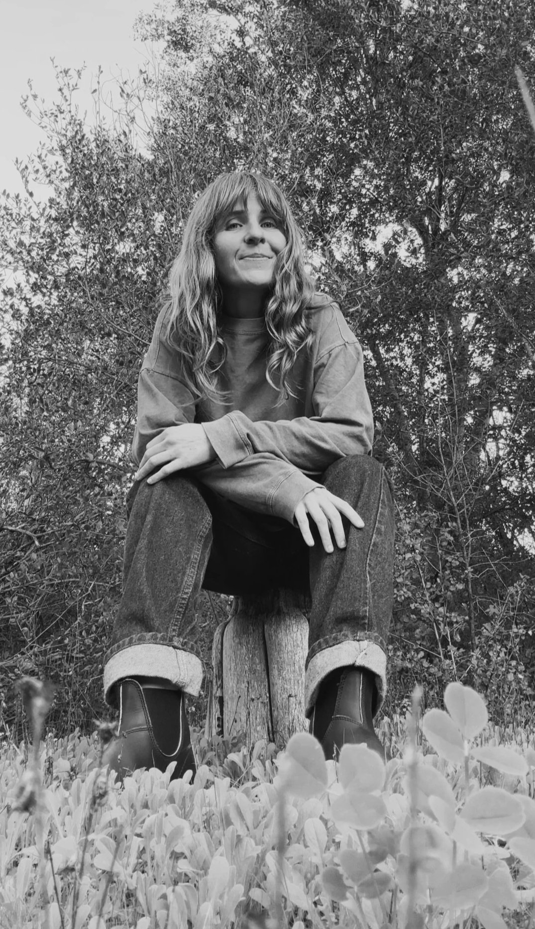 Portrait of Danny Kantrowitz, psychodynamic psychotherapist, sitting on a tree stump from a former orange orchard in Ojai, California, surrounded by native and volunteer plants reclaiming the land as home and wildlife habitat-- the future office site