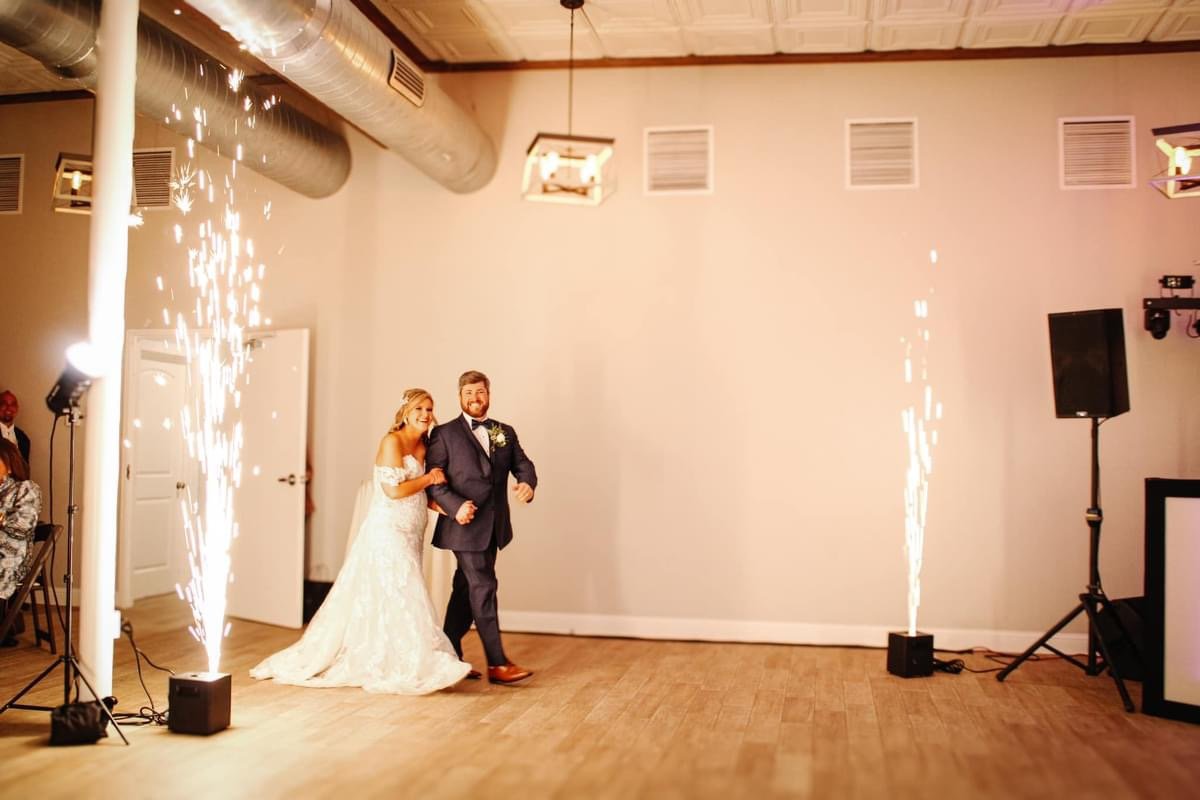 Bride and groom dancing at their wedding reception with sparklers and fireworks displays in the background.
