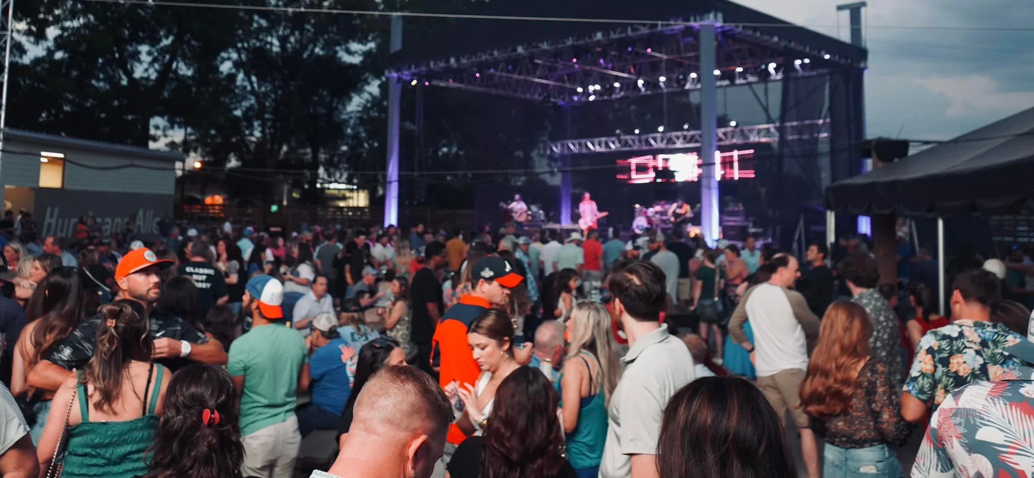 Crowd of people at an outdoor concert during dusk, facing a stage with live band performance and a digital countdown display.