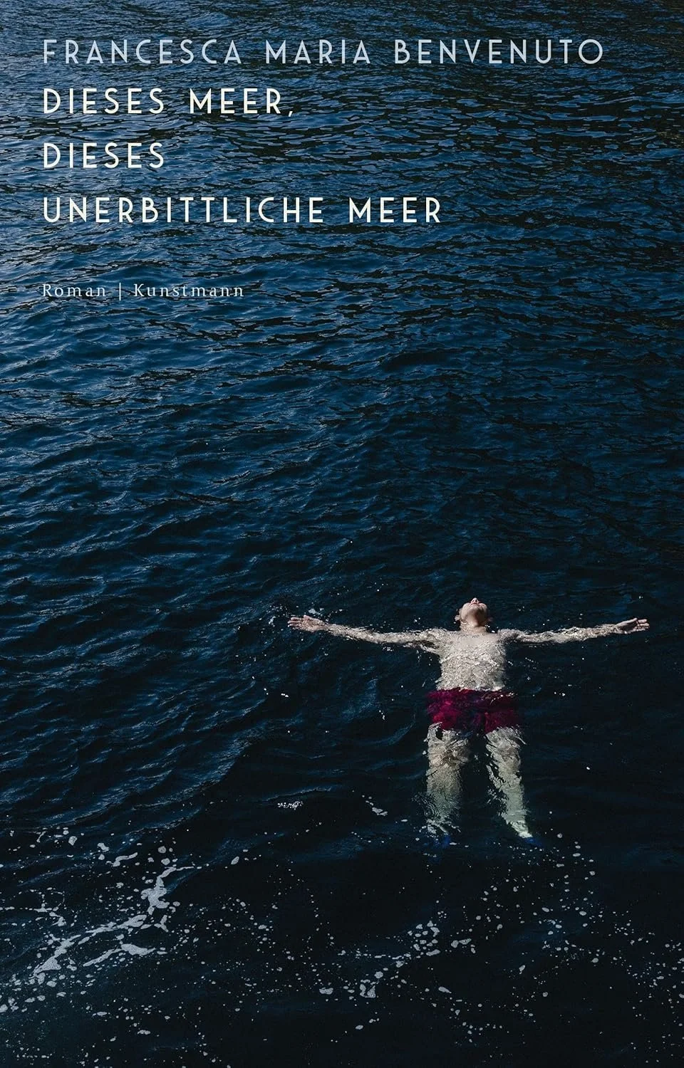 Person swimming in the ocean with arms and legs outstretched, wearing red shorts and facing upward. Text in German overlaying the water reads: 'Francesca Maria Benvenuto, dieses Meer, dieses unbittliche Meer, Roman | Kunstmann'.