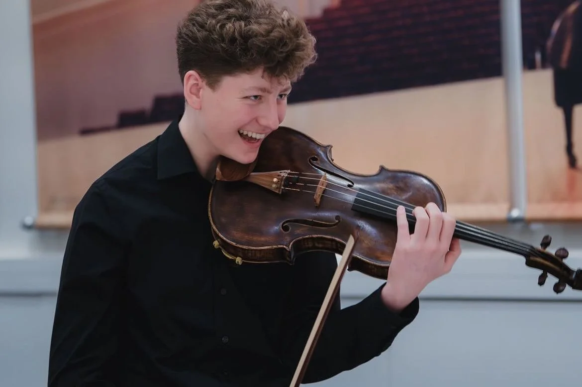 Young man playing the violin, smiling, indoors.