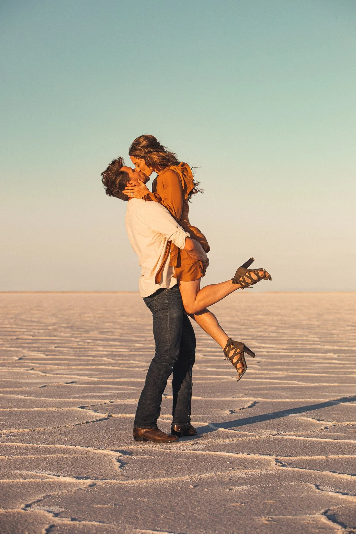 A man lifting a woman in a desert landscape as they kiss.