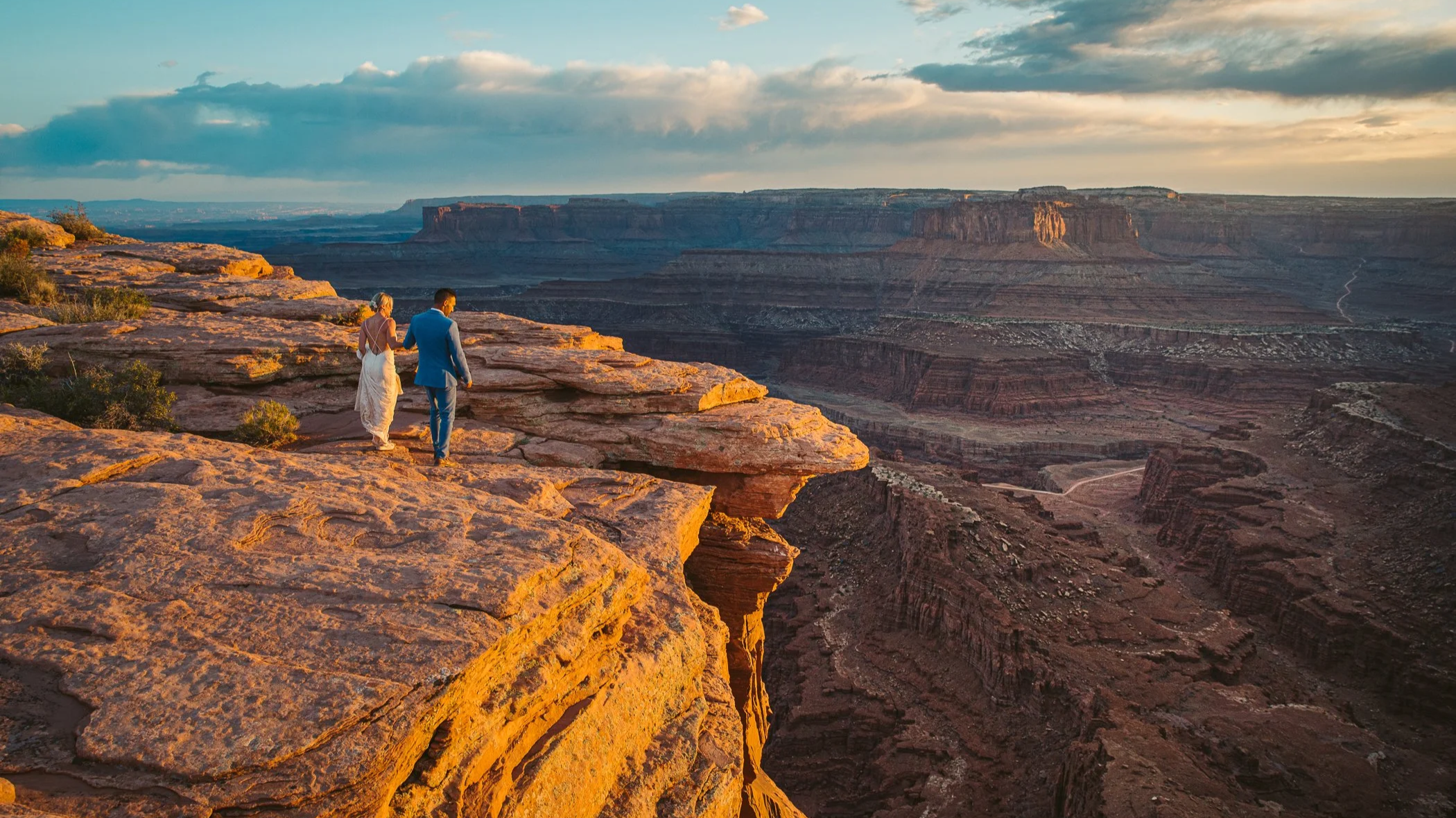 A couple walking on the edge of a rocky cliff overlooking the Grand Canyon during sunset.