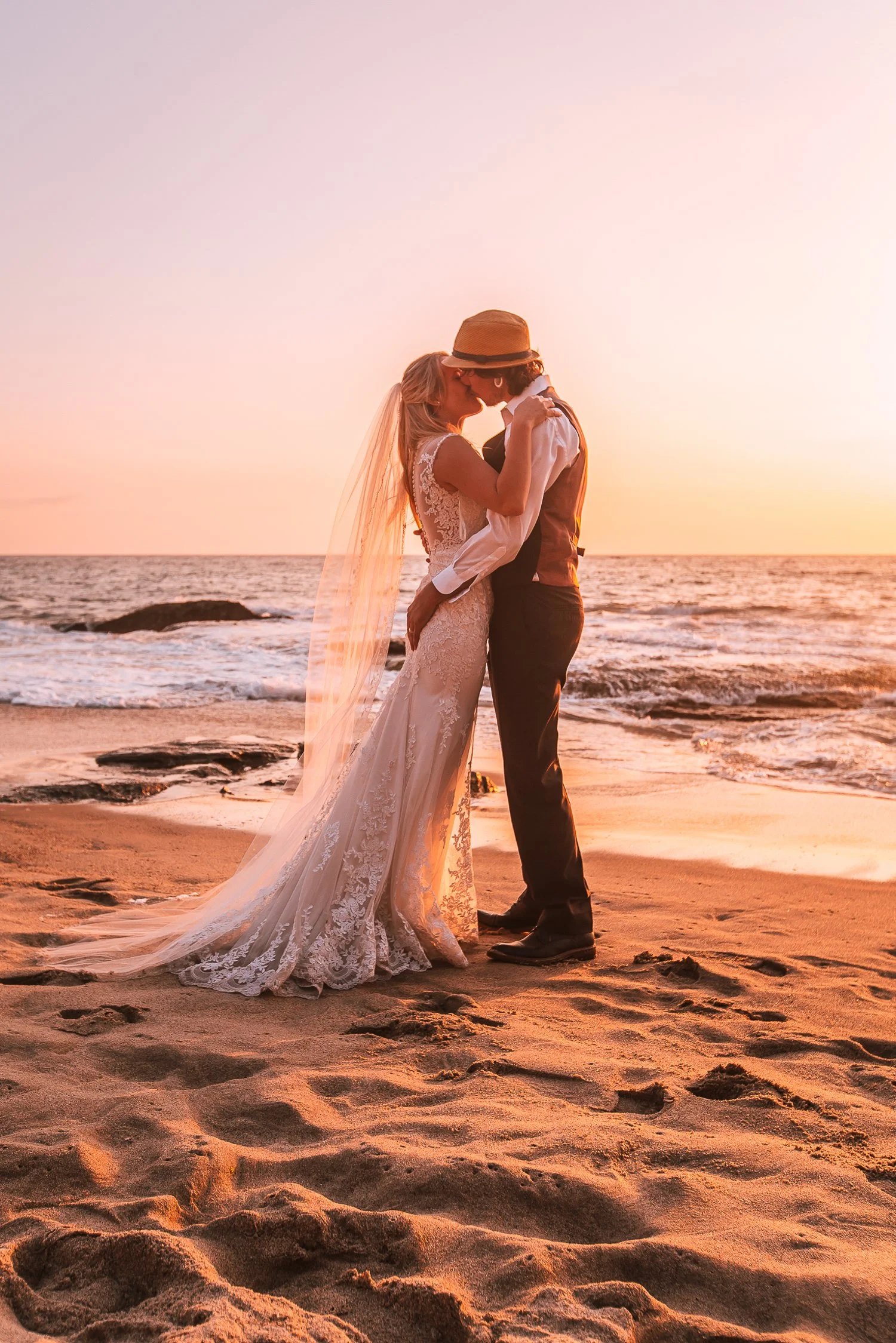 A bride and groom sharing a kiss on the beach at sunset.