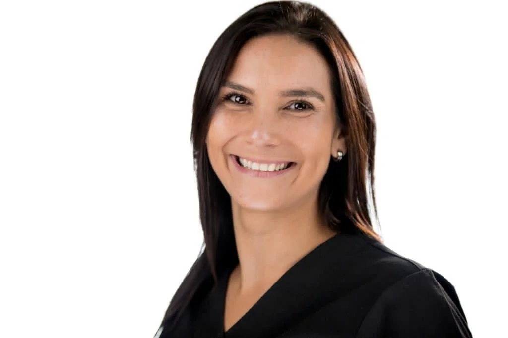 A woman with shoulder-length dark hair, smiling, wearing a black top, against a plain white background.
