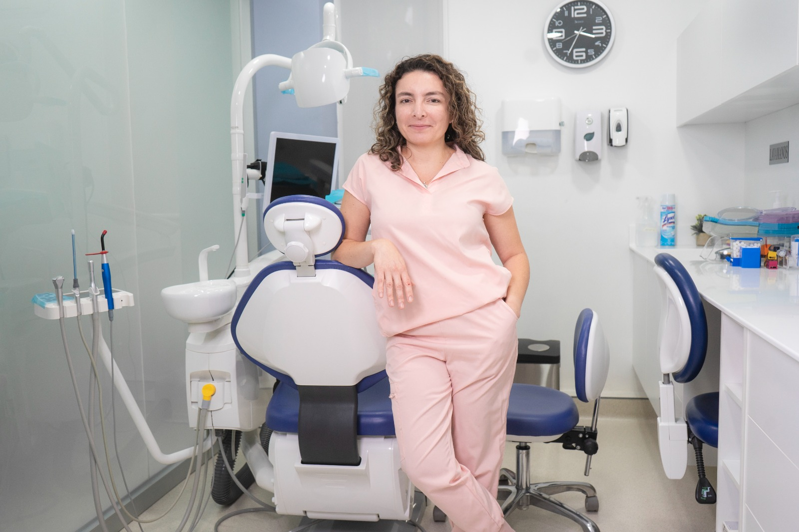 A woman in a pink dental uniform leaning on a dental chair in a modern dental clinic.