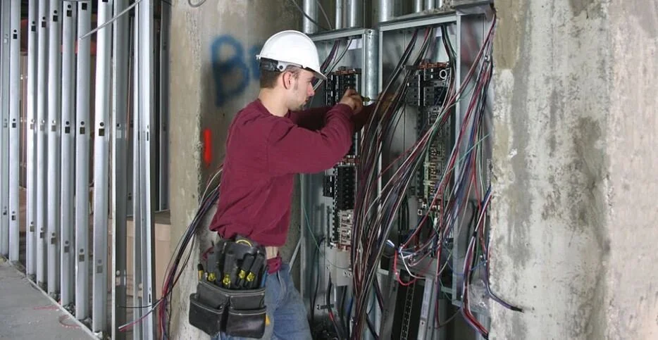 A technician working on an electrical panel with wires in a building under construction.