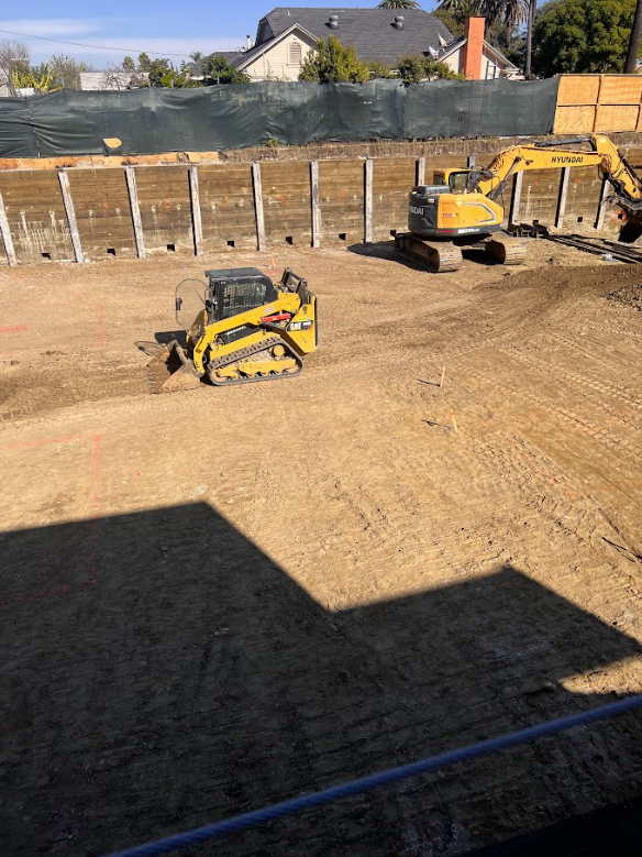 Construction site with small yellow excavator and a larger yellow excavator working on leveling the ground.