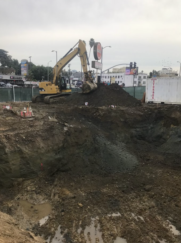 Construction site with an excavator digging a large hole in the ground in an urban area.