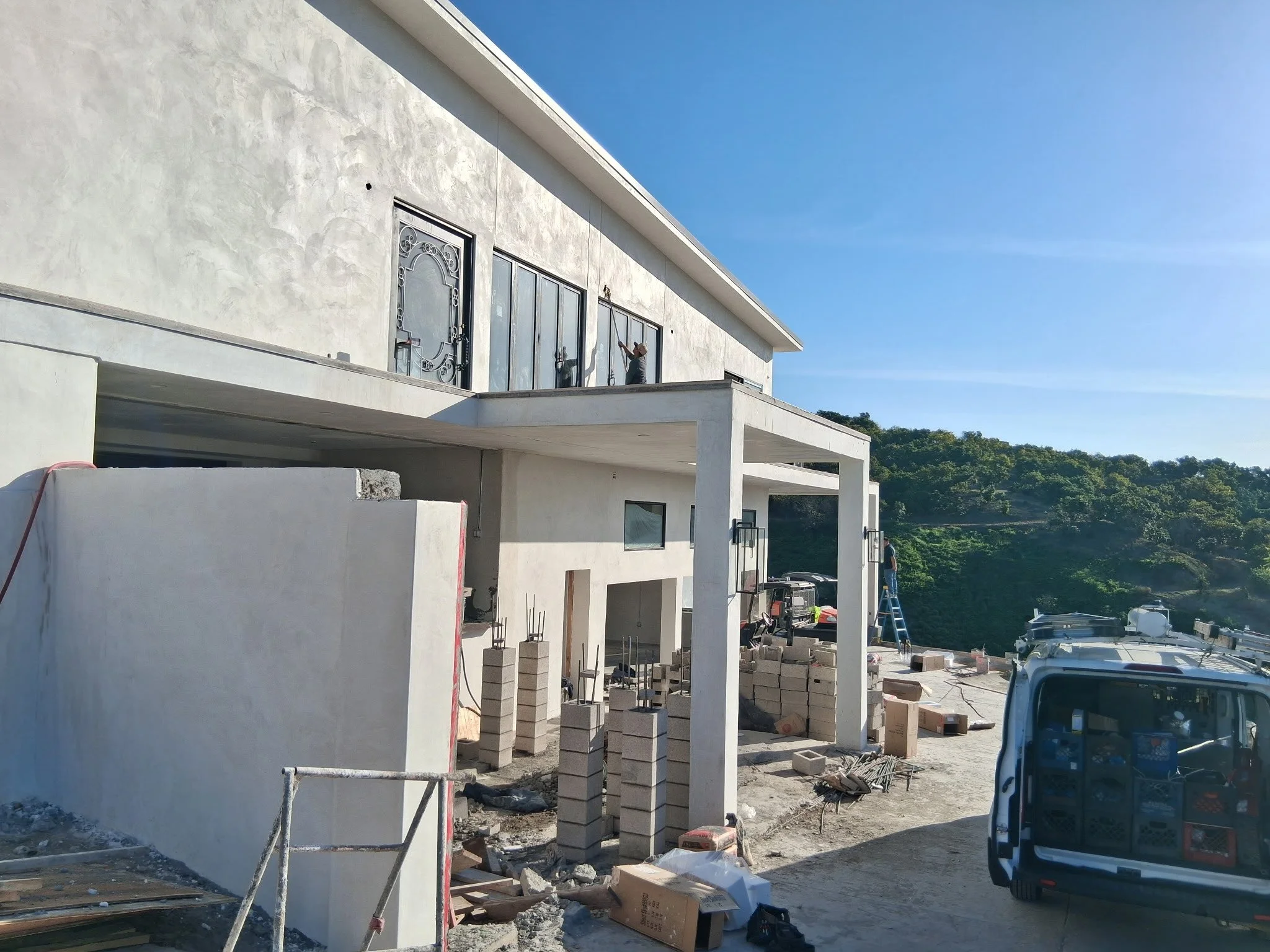 Another Angle of our Customer Residential Construction site with workers, building walls, and a van in a hilly area under a clear blue sky in Somi's California by AY Builders Los Angeles