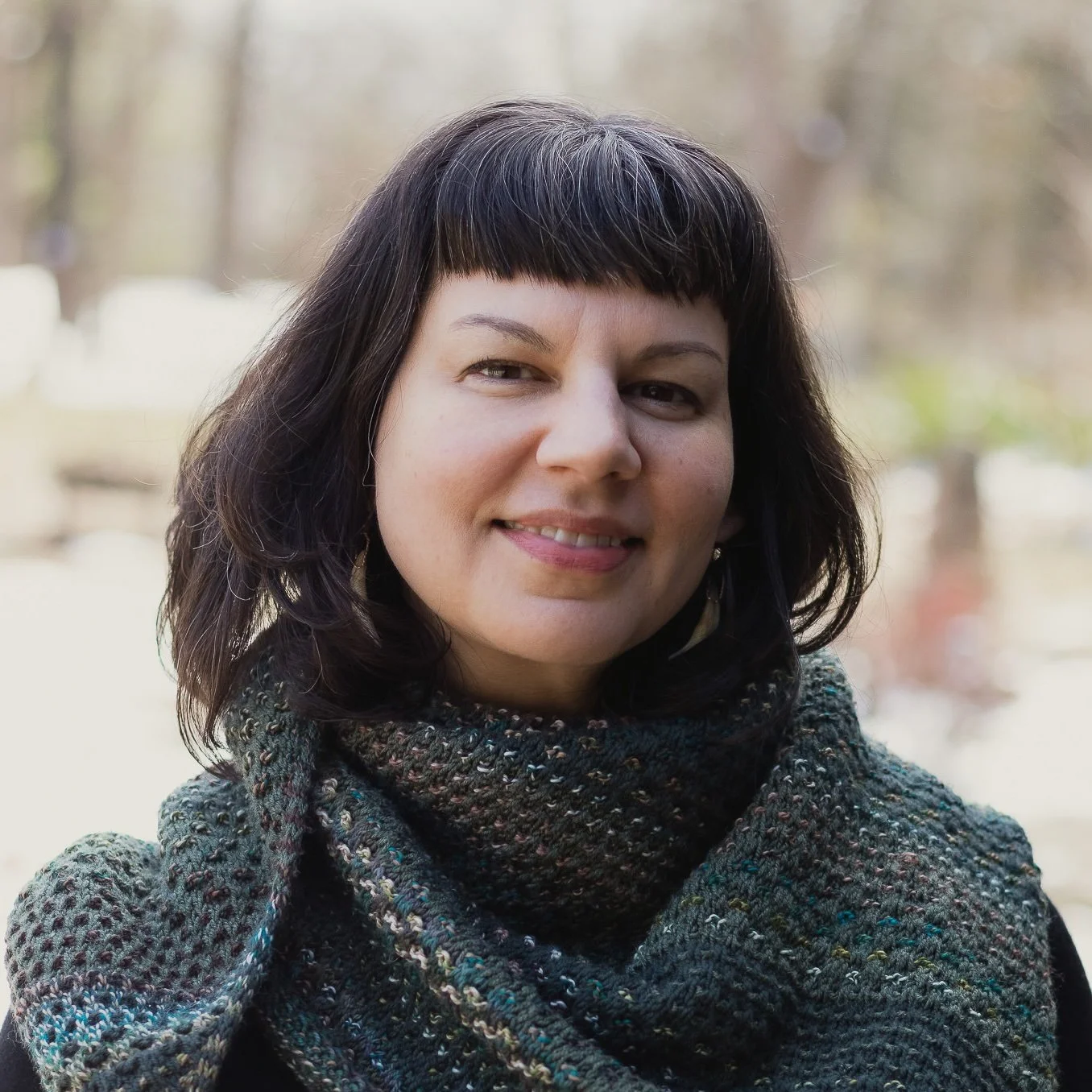 Monica Basile smiling outdoors with a hand knit scarf
