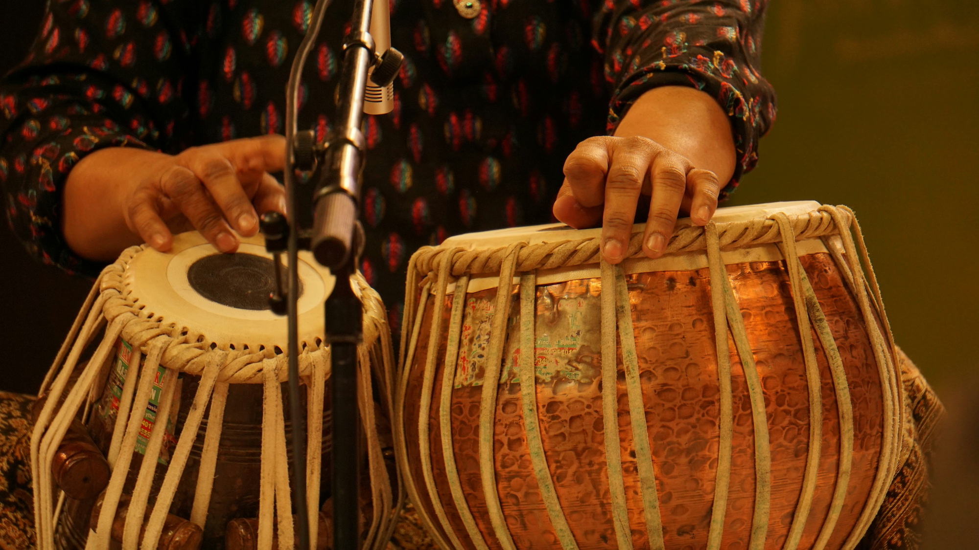 Close-up of a person playing wooden drums with their hands, with a microphone nearby.