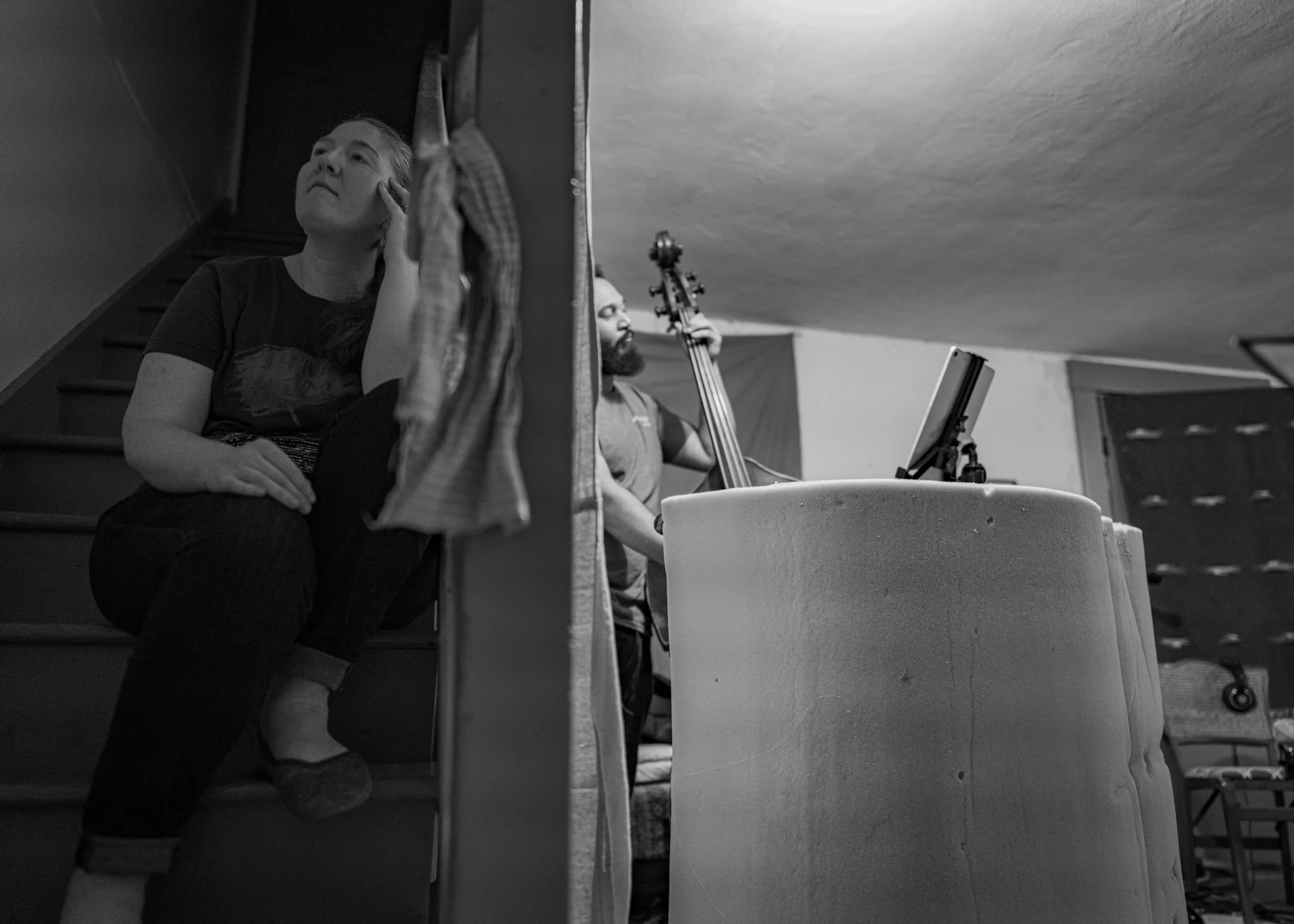 Two people in a room at the Esteban recording session, one sitting on stairs and another playing cello.