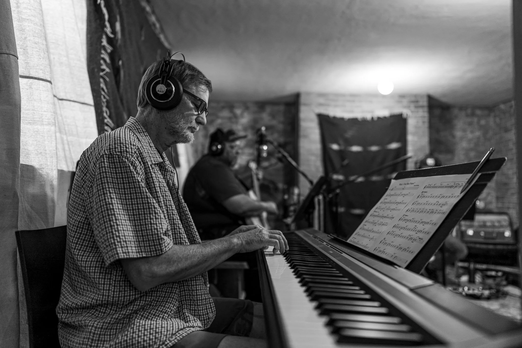 John Rapson playing a digital piano for the Esteban recording session, wearing glasses and headphones, with a music sheet on the stand.