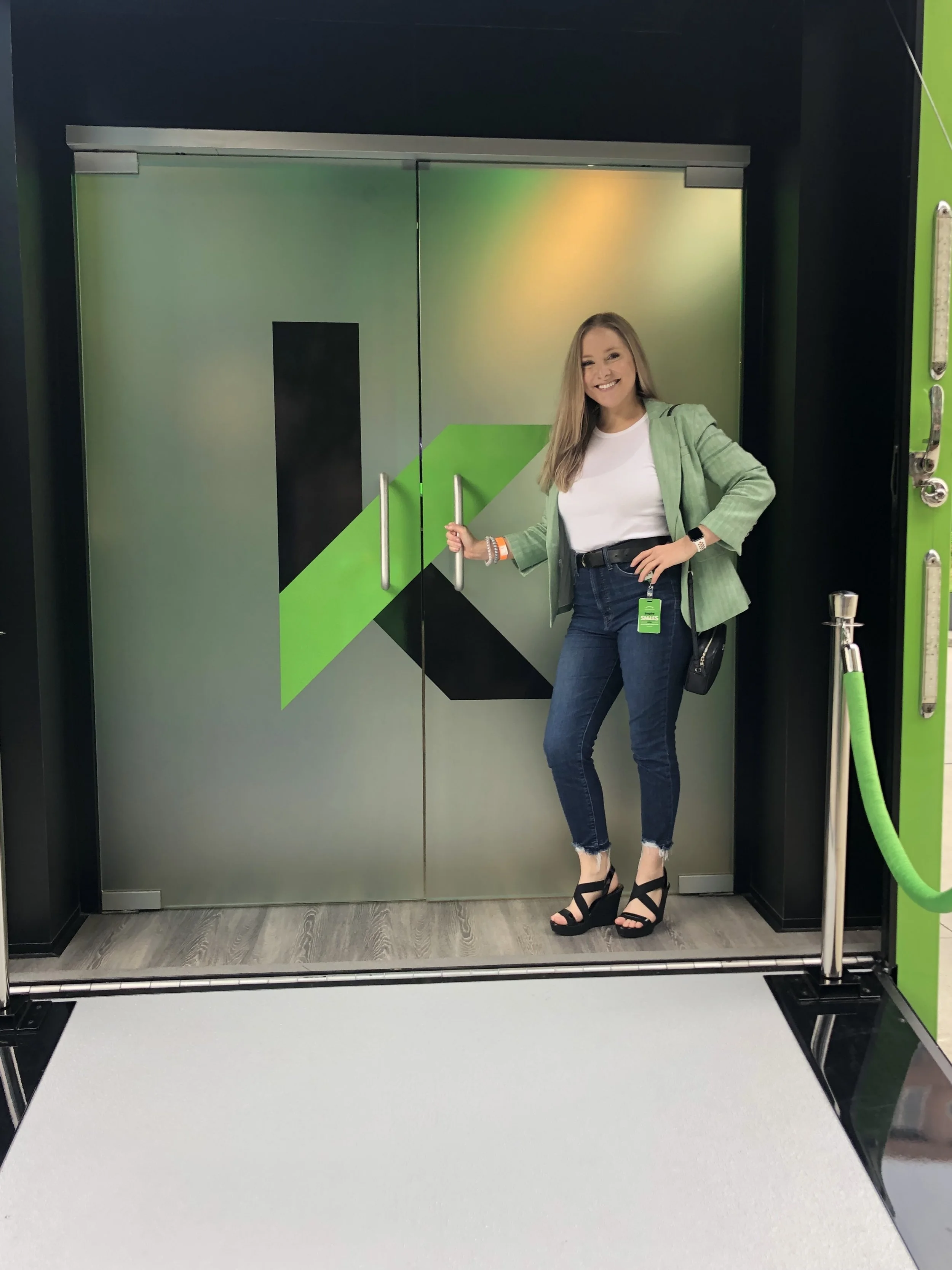Woman standing in front of a large sliding door with a green, black, and gray geometric design, holding the door handle and smiling.