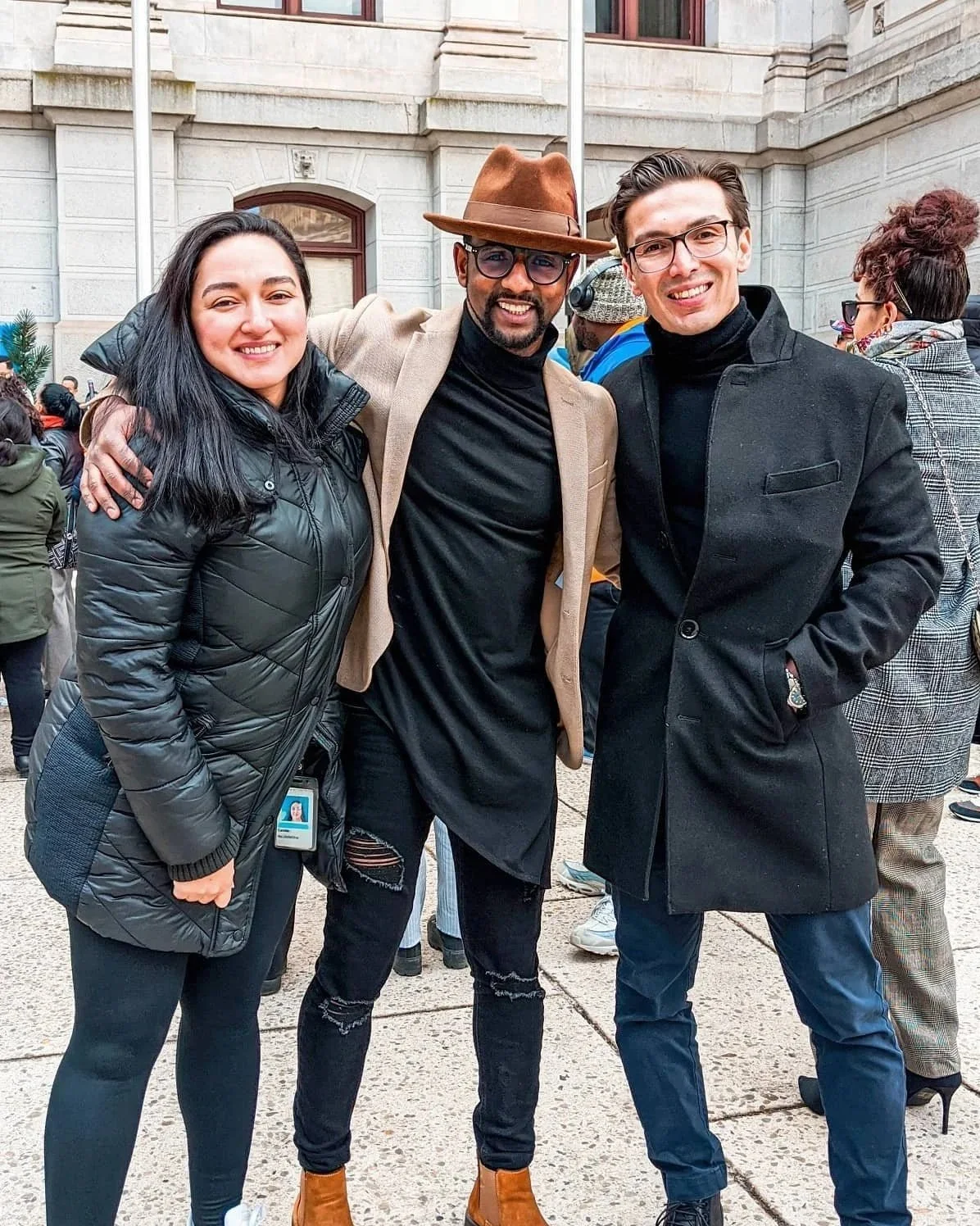Three people standing outdoors in front of a historic building, posing for a photo and smiling.