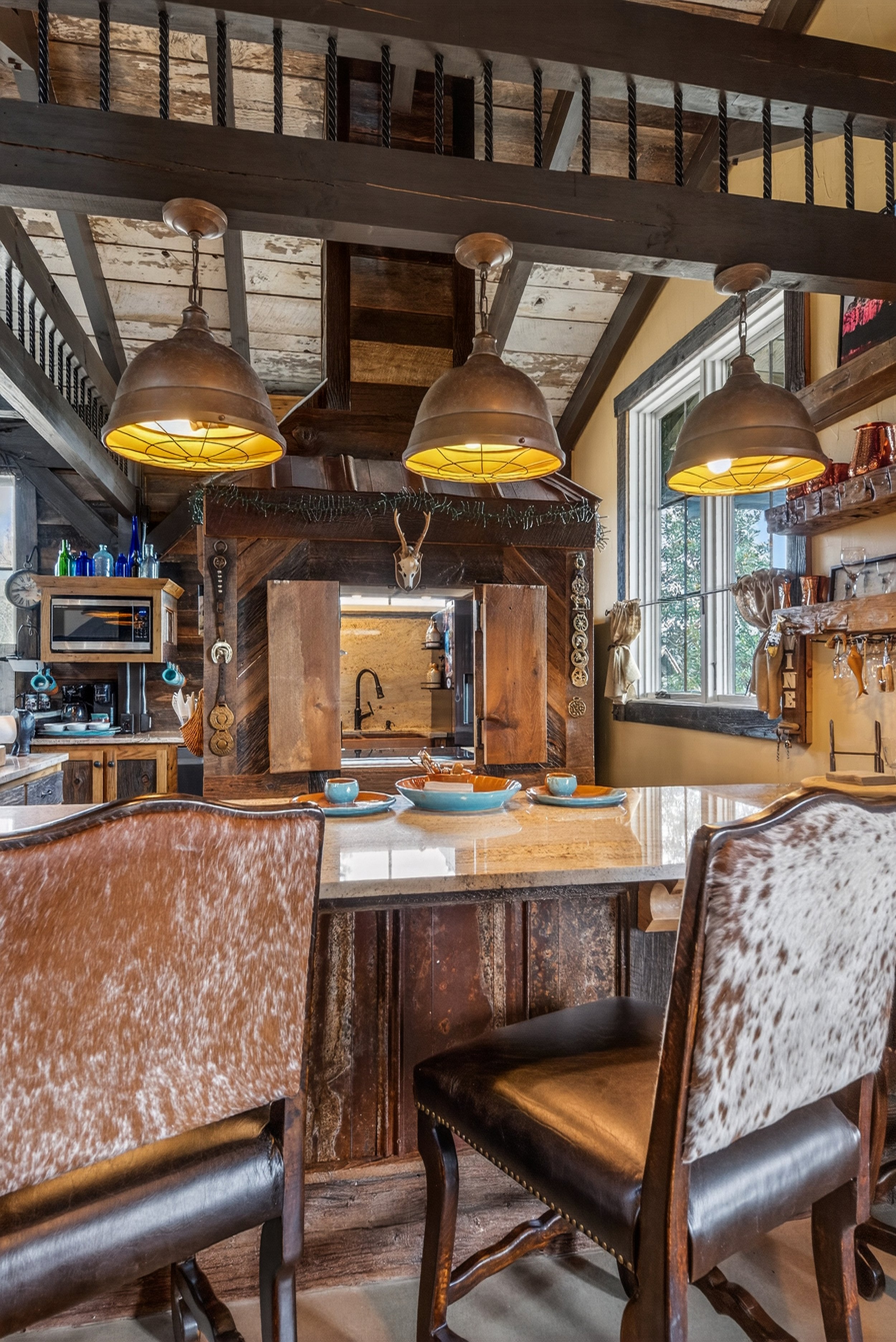 Rustic kitchen with a wooden island, two leather chairs, and three pendant lights hanging from a loft ceiling.