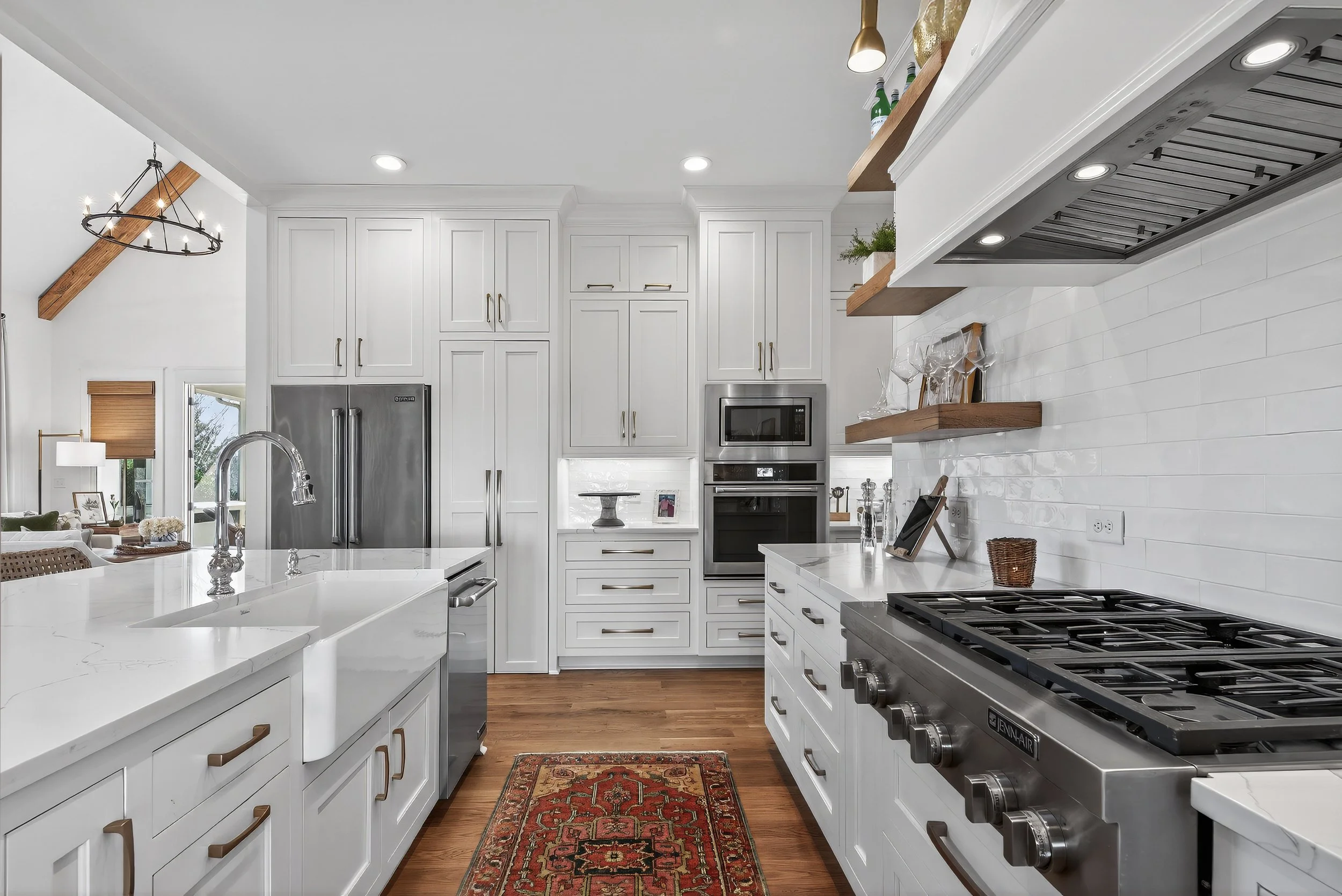 Modern white kitchen with stainless steel appliances, wood shelves, and a wooden floor.
