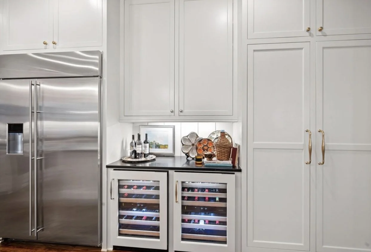Kitchen cabinet area with a stainless steel refrigerator, white cabinets, a wine cooler, and decorative items on the counter.