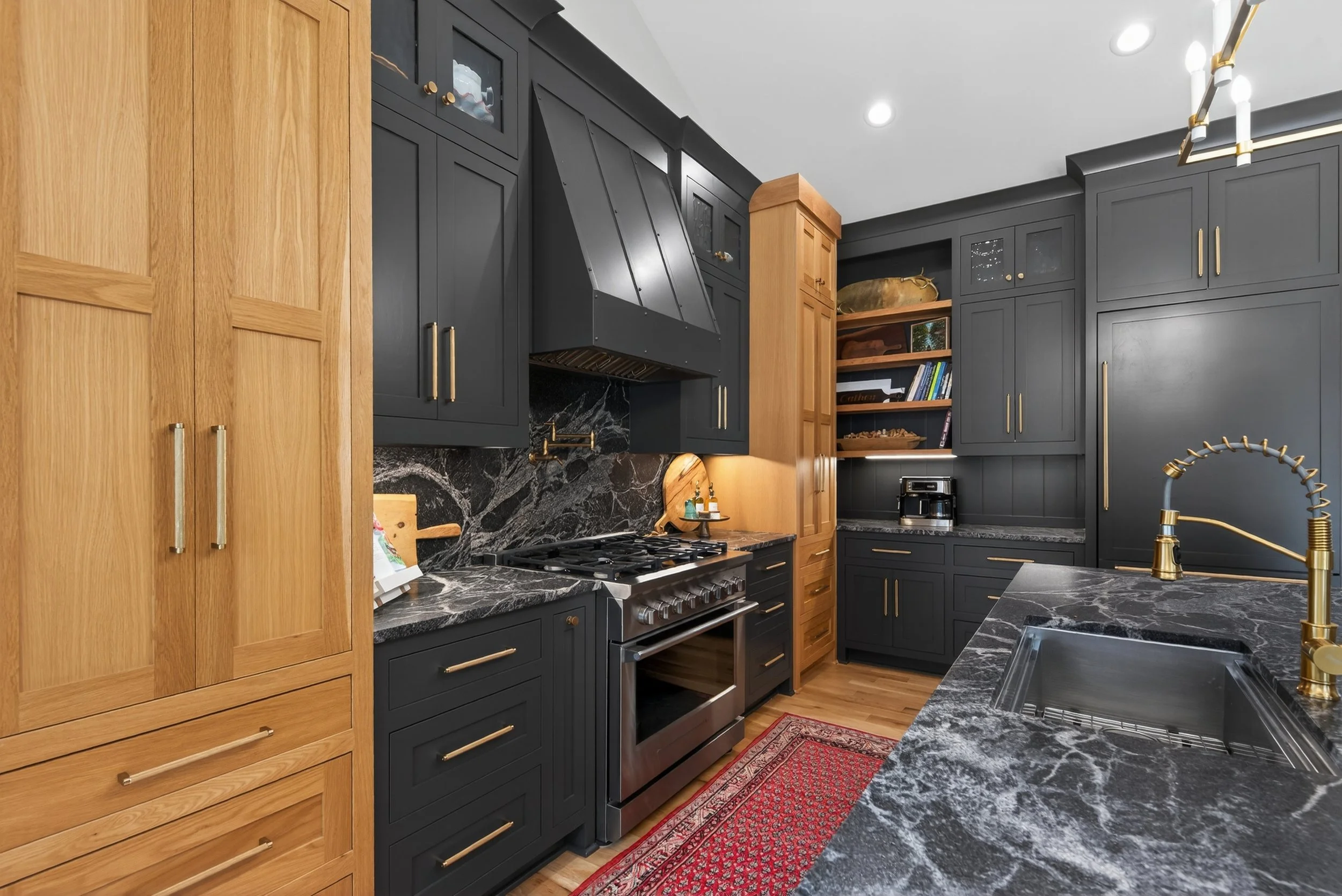 Modern kitchen with black and natural wood cabinets, black marble countertops, a stainless steel stove, and gold hardware and fixtures.