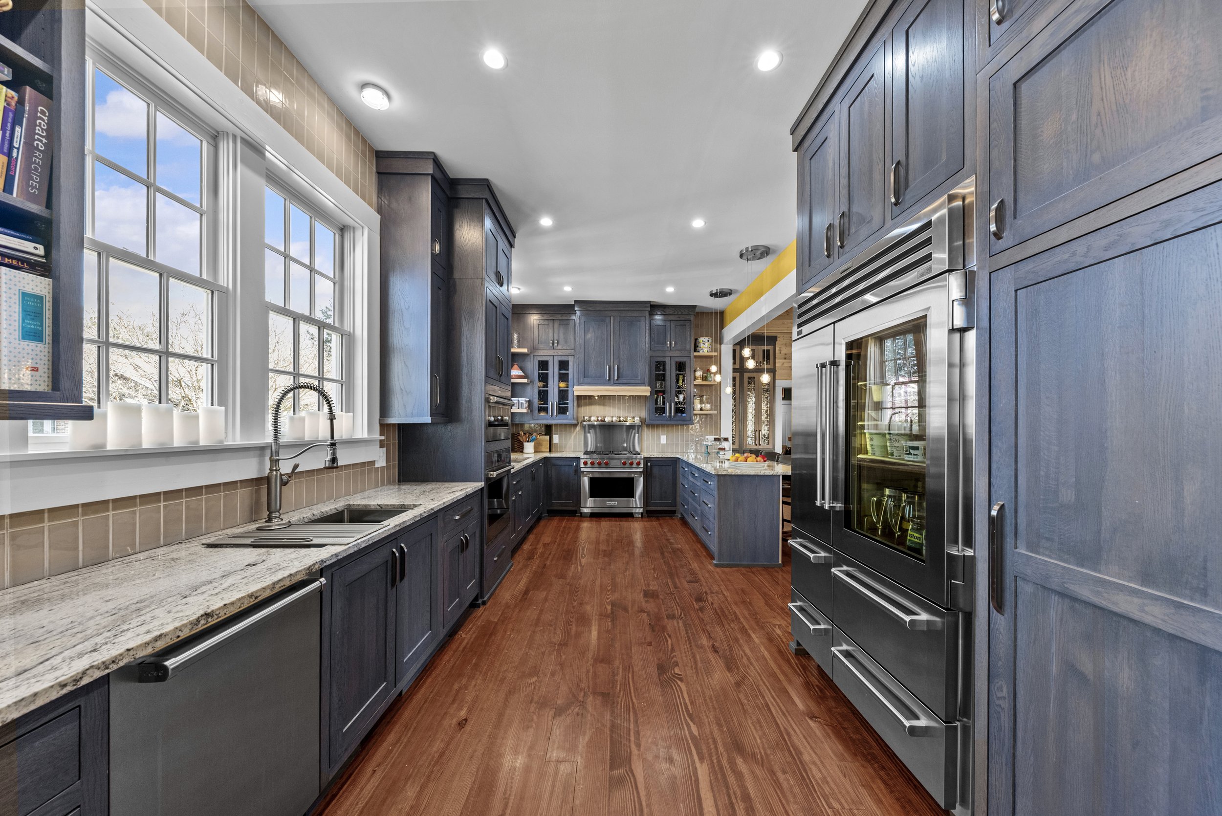 Modern kitchen with dark blue cabinets, granite countertops, and hardwood floors. Large window above sink, built-in stainless steel appliances, and a yellow trim on the ceiling.