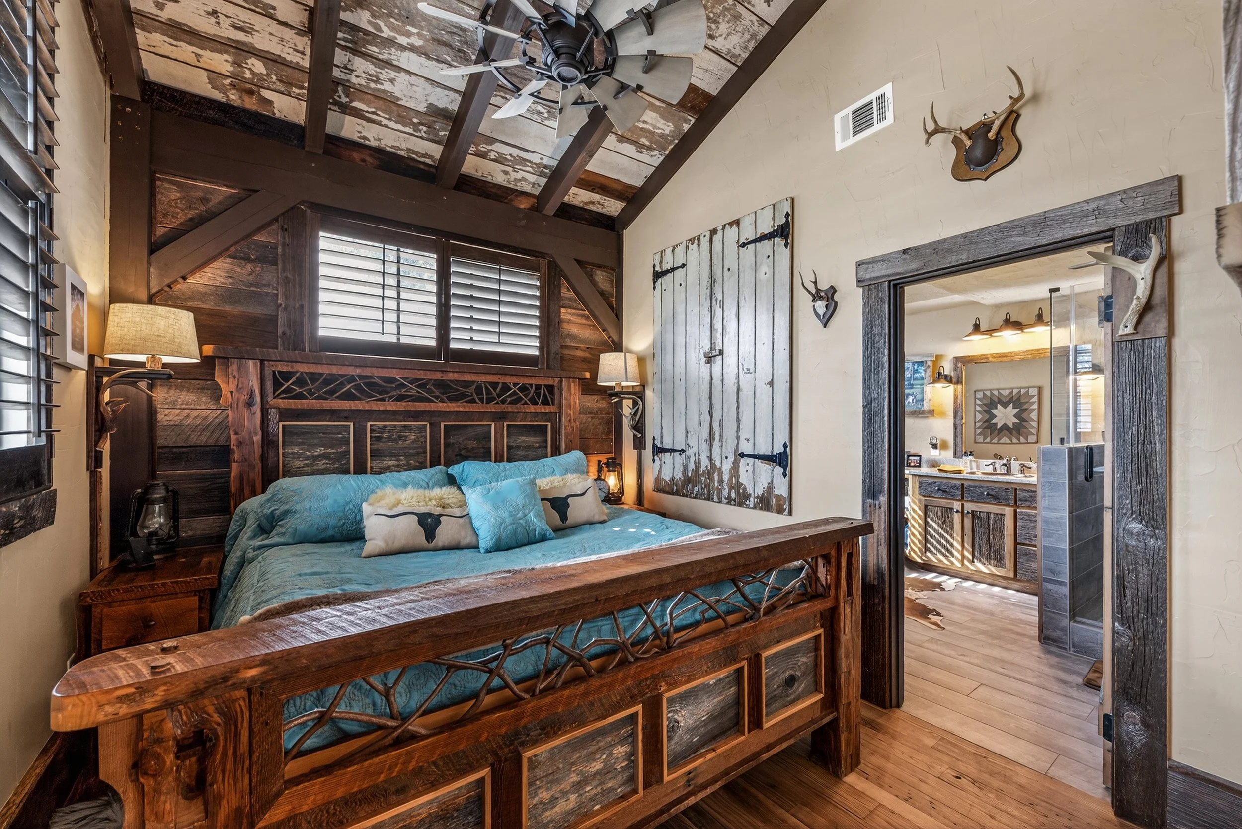 Rustic bedroom with wooden furniture, blue bedding, and antler decorations on the wall.
