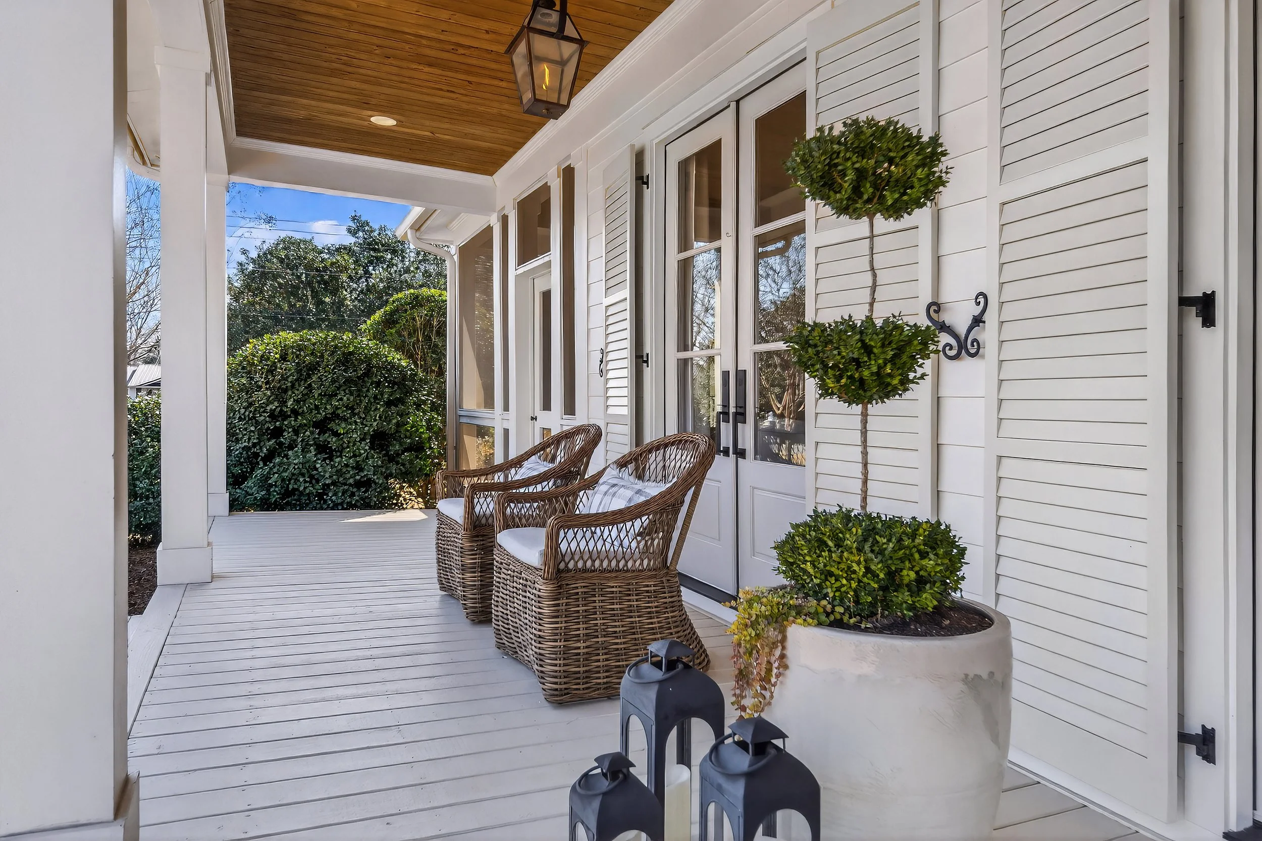 Porch with wicker chairs, potted topiary, and decorative lanterns in a sunny outdoor setting.