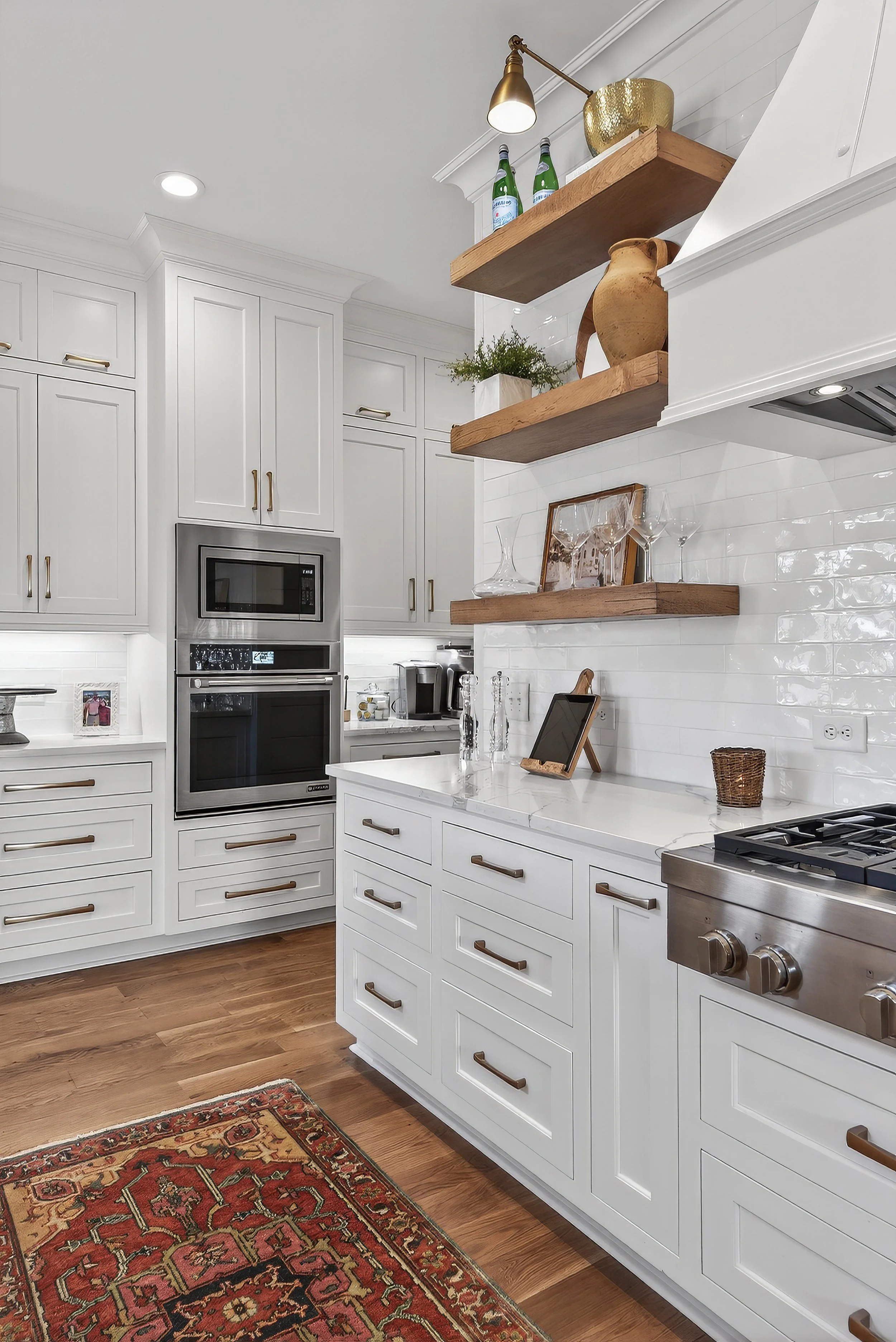 White kitchen with wooden open shelves holding bottles, vases, and decorative items, stainless steel appliances, hardwood flooring, and a red patterned rug.
