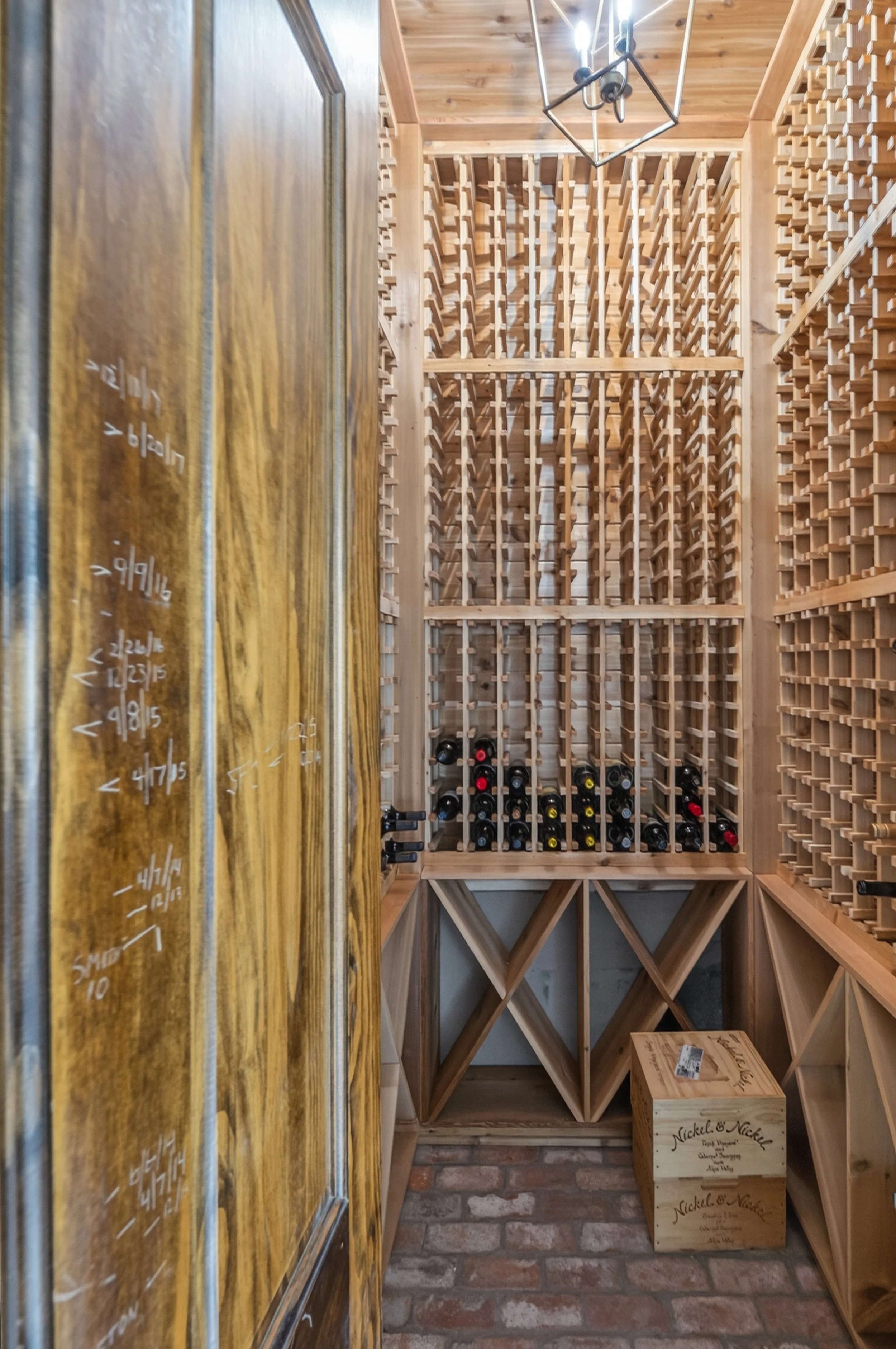 A wine cellar with wooden racks filled with wine bottles, a brick floor, and a wooden box on the floor.