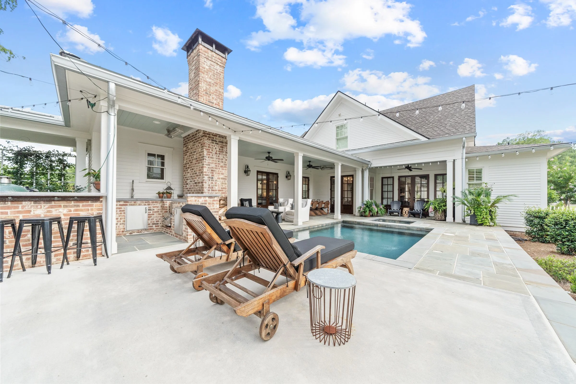 Backyard with a small swimming pool, poolside lounge chairs, and a covered patio area with outdoor seating, plants, and string lights