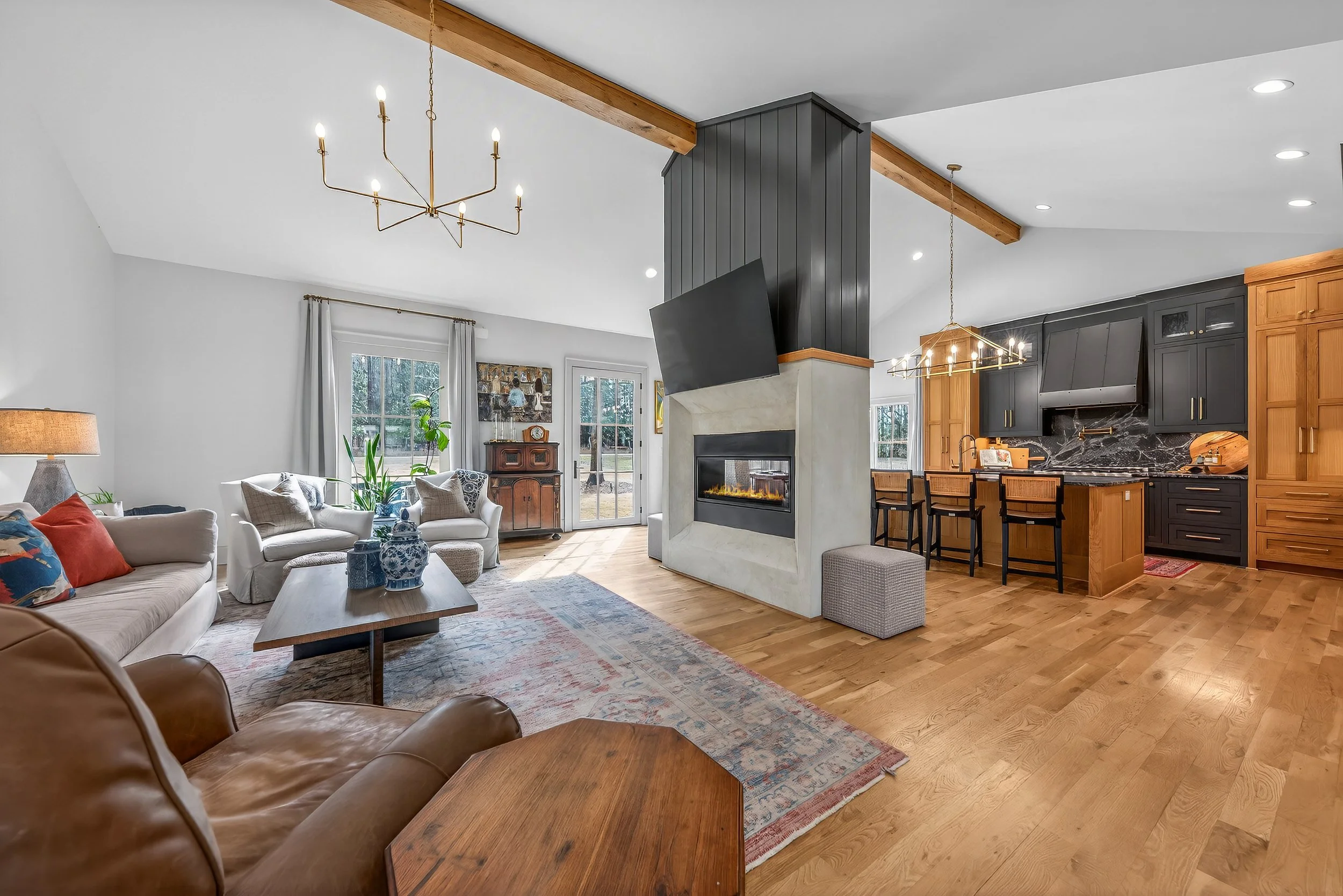 Open-concept living room and kitchen with hardwood floors, white walls, large windows, and modern furnishings.