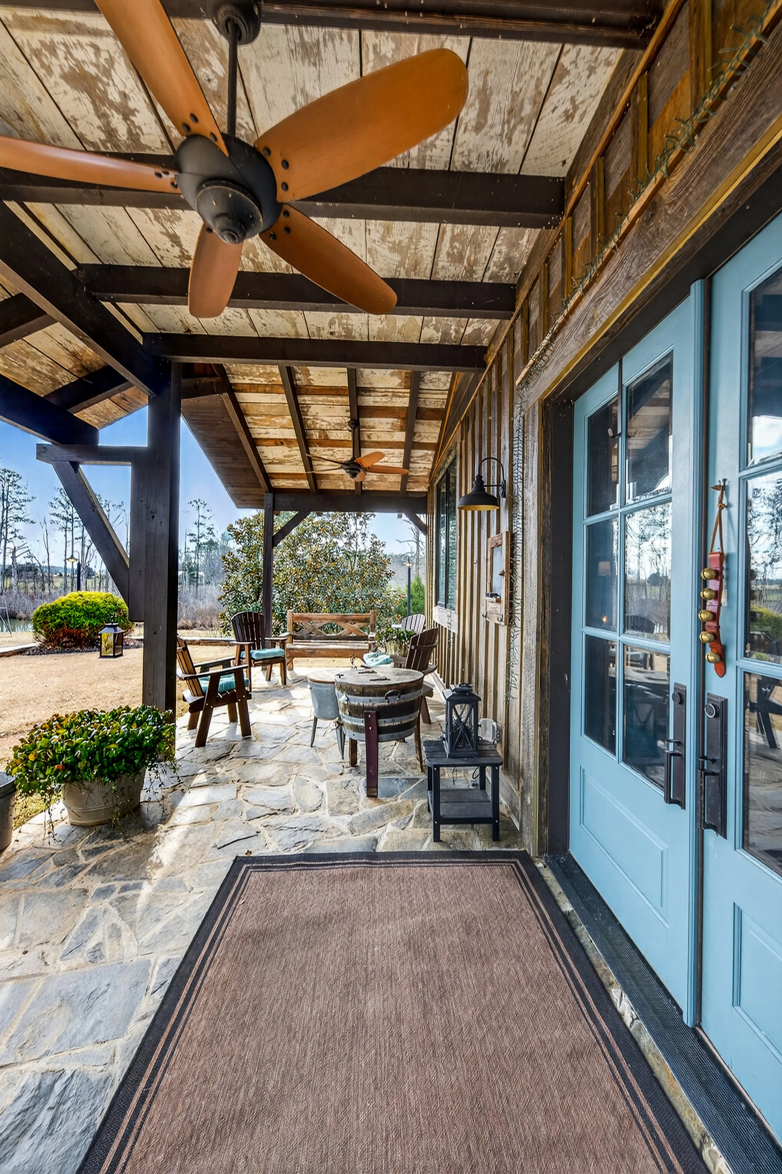 Covered porch with seating area, ceiling fans, blue front door, and potted plants.