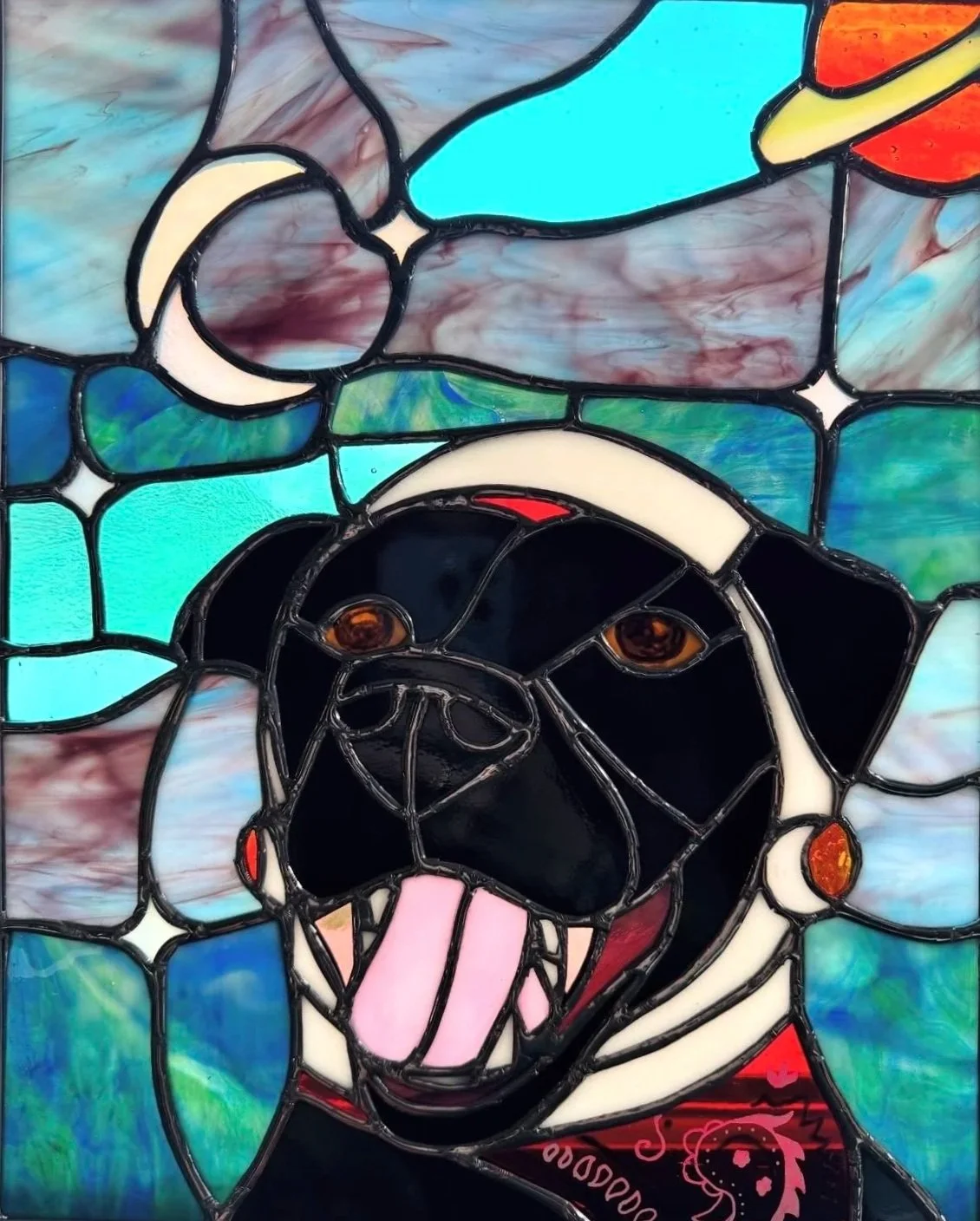 Stained glass window depicting a stylized face, with a black background, orange eyes, open mouth with a pink tongue, and various colorful abstract shapes.