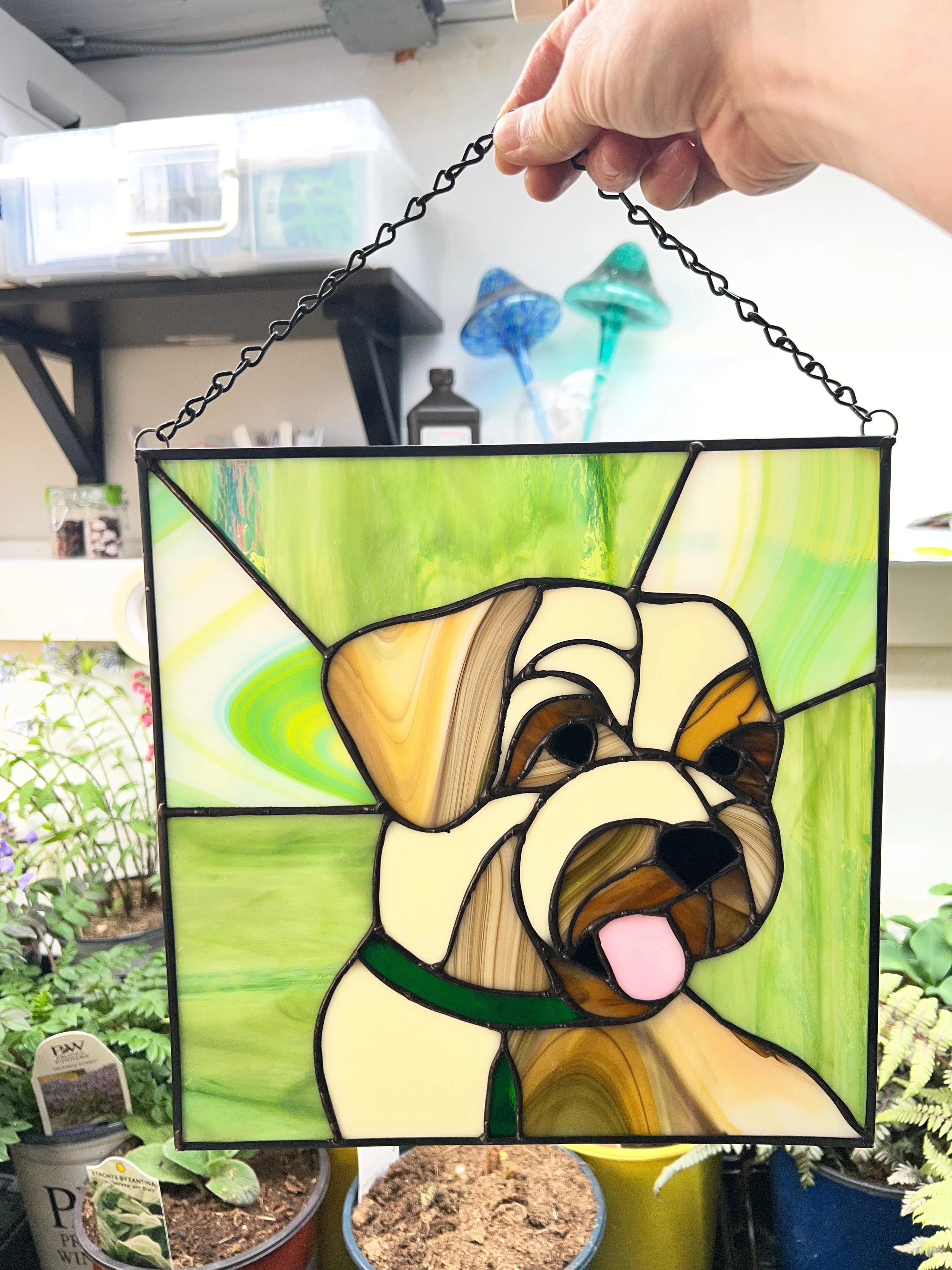 Colorful stained glass lantern with a koala bear design, hanging outdoors among potted plants.