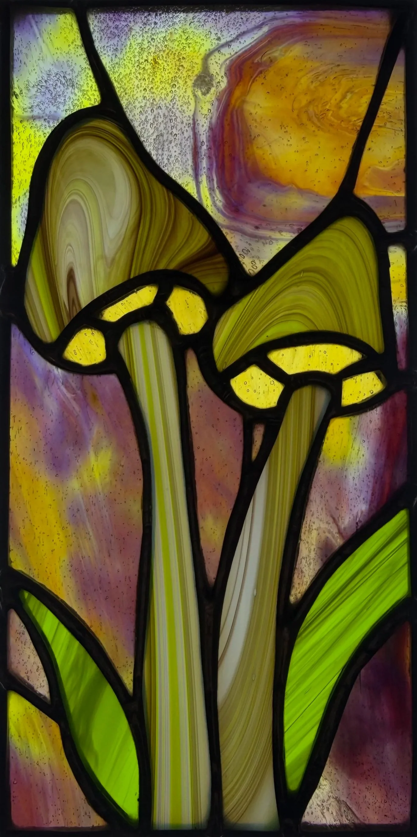 Colorful stained glass window featuring an abstract design with flowing yellow, green, purple, and orange shapes separated by black outlines.