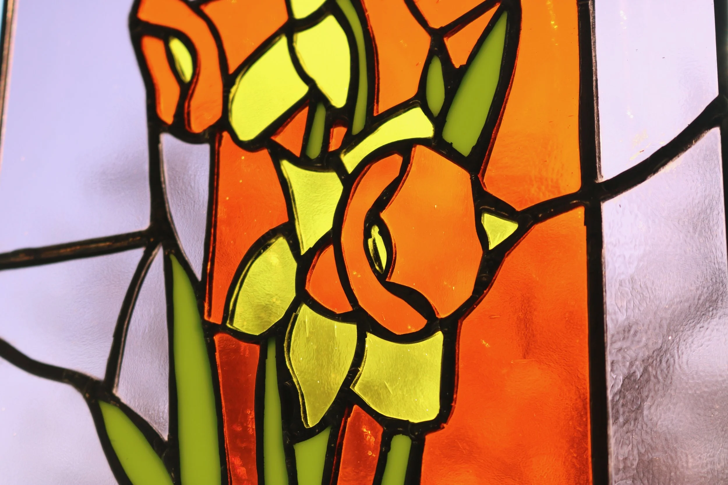 Close-up of a stained glass window featuring an orange flower with green leaves.