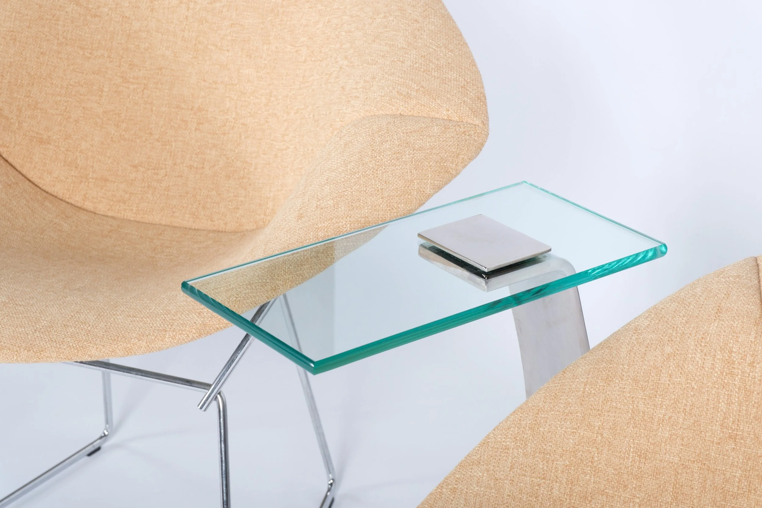 c-shaped side table with glass tabletop and nickel leg and base, close up next to cream chairs