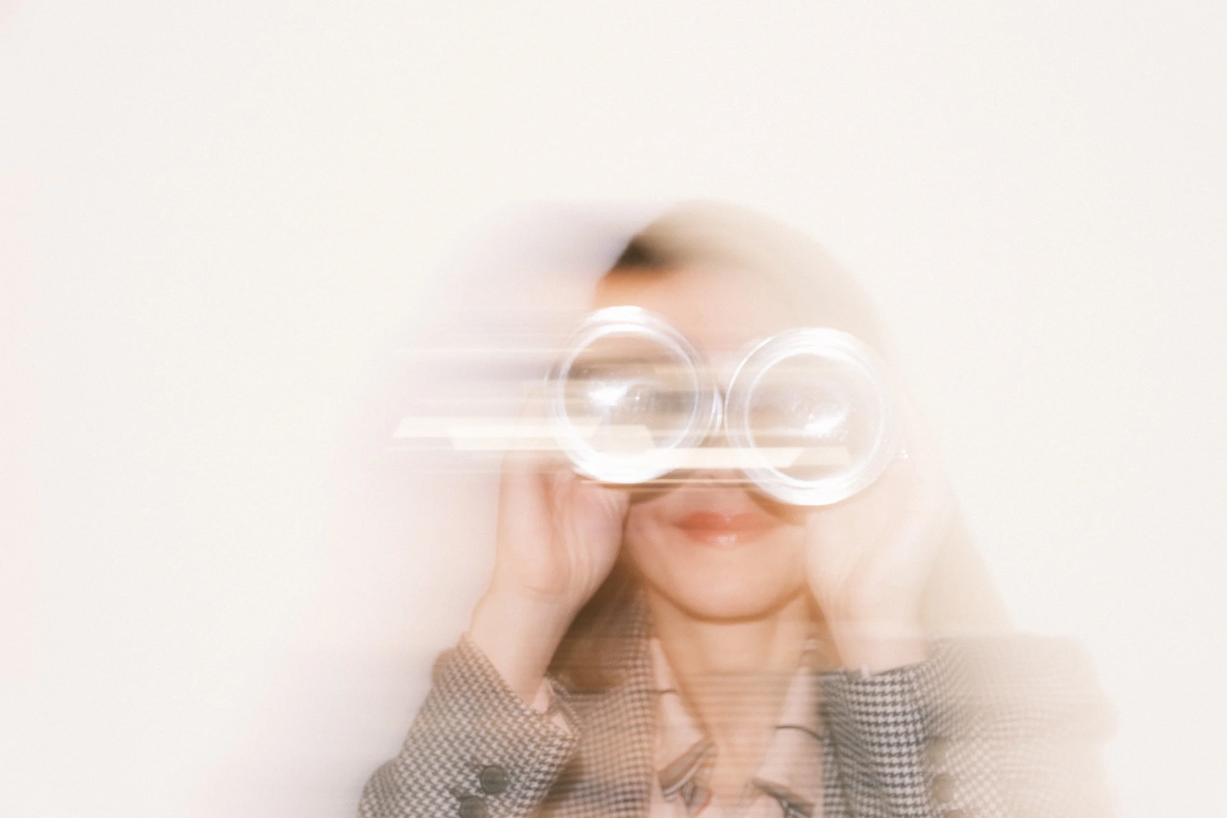 blurred woman playfully holding up lightbulbs to her eyes like binoculars