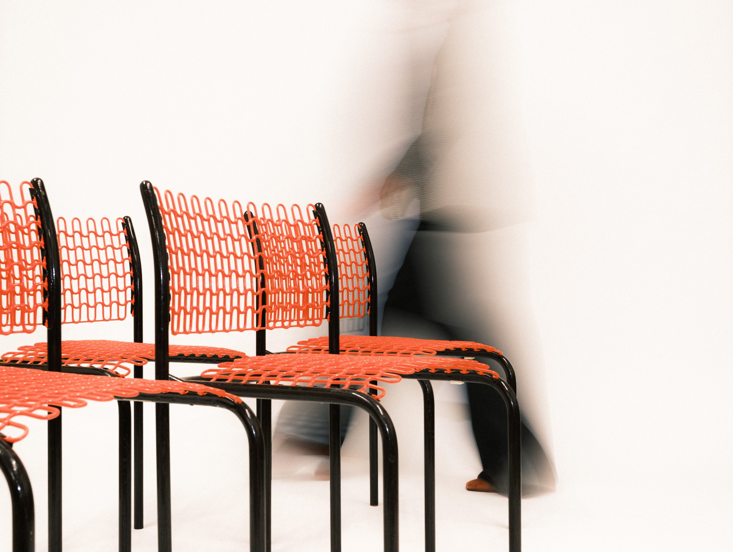 blurred woman walking past vintage coral and black wire chairs