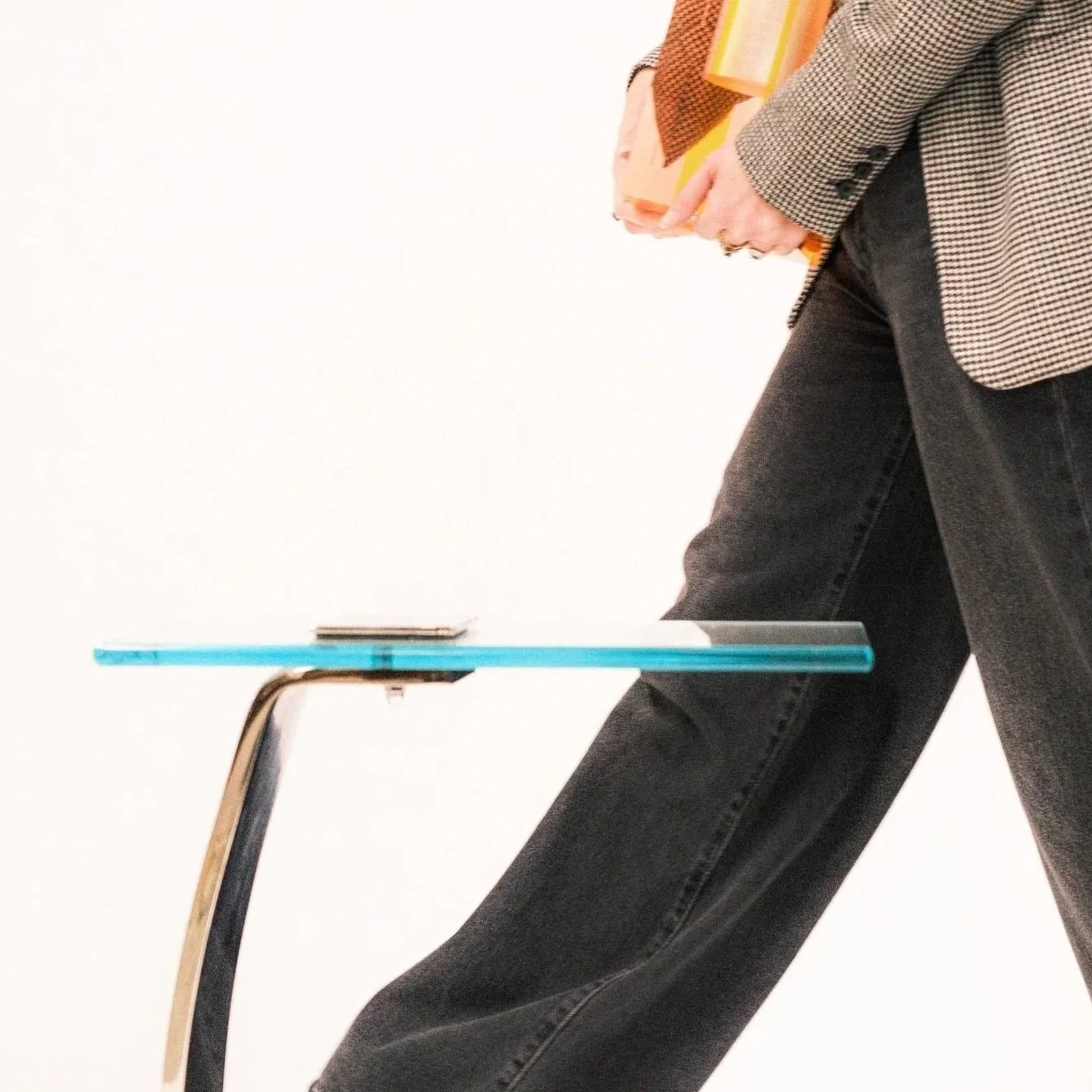 woman walking behind glass and nickel c-shaped side table against white backdrop