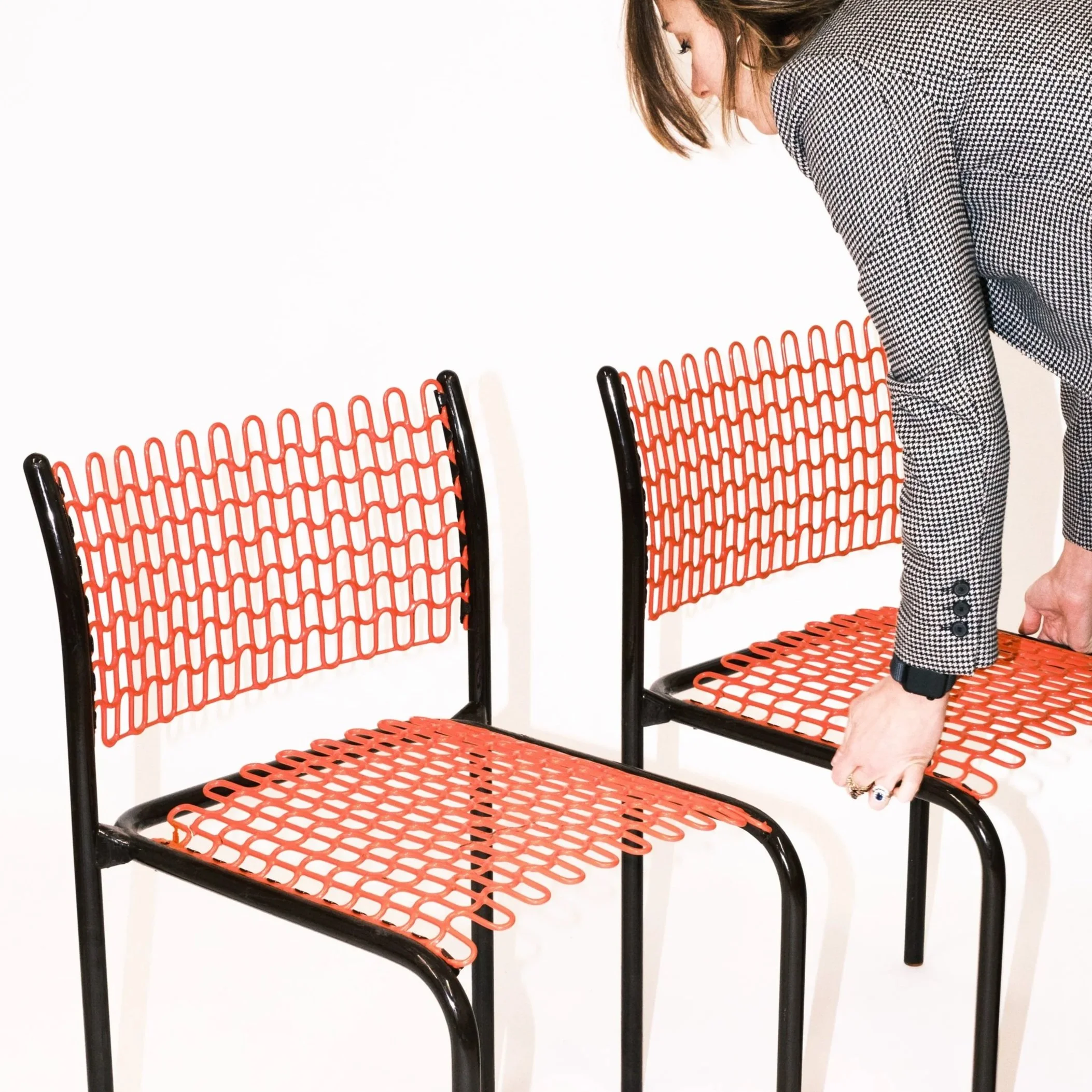 woman placing coral and black wire chairs against white backdrop