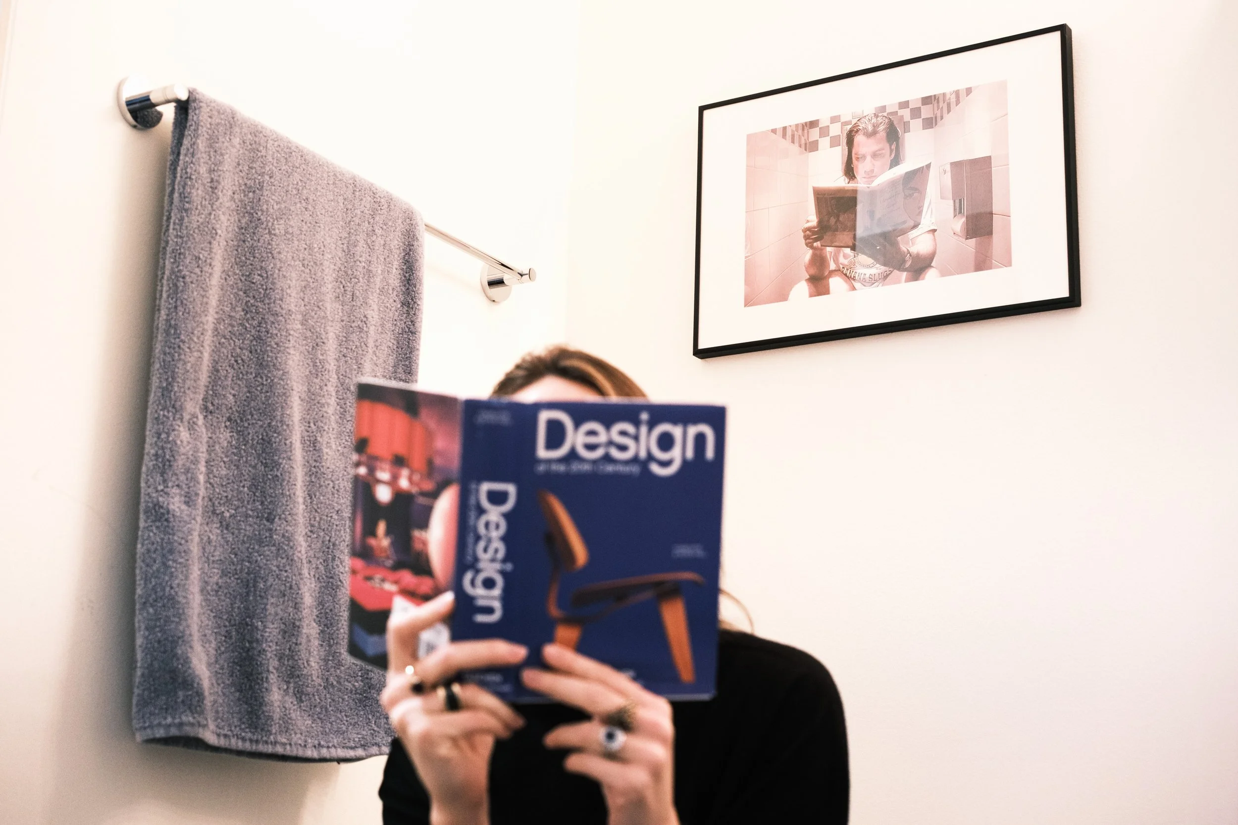 woman reading book in bathroom imitating scene in the movie Pulp Fiction, with framed image of that scene on the wall in the background