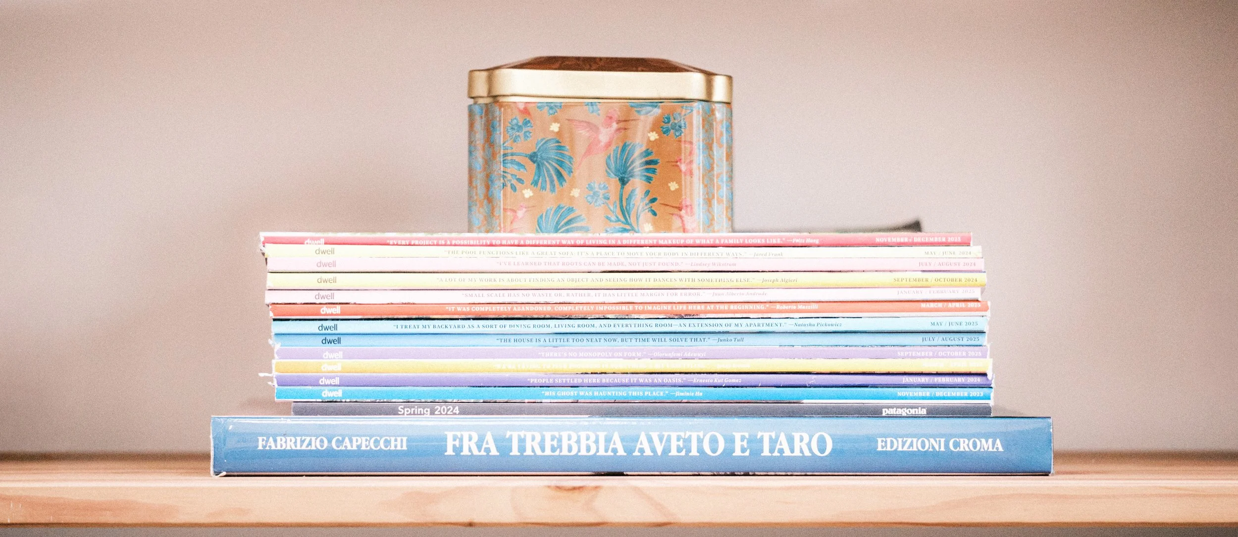 vintage decorative tin placed on top of stack of old dwell magazines on bookshelf