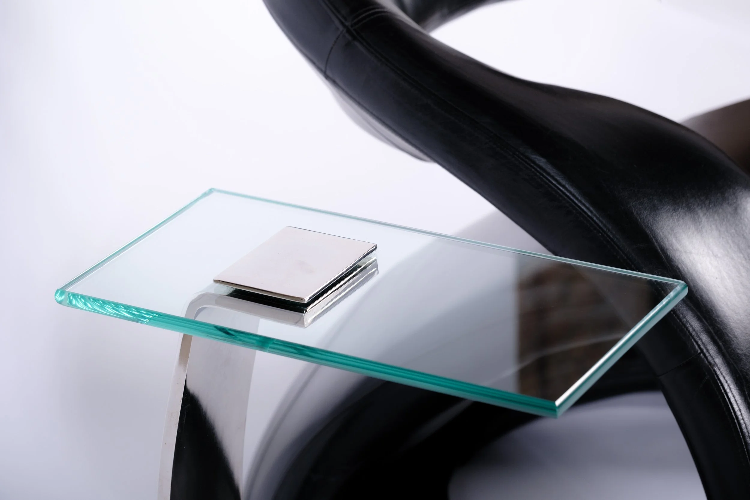 c-shaped side table with glass tabletop and nickel leg and base, close up next to black chair