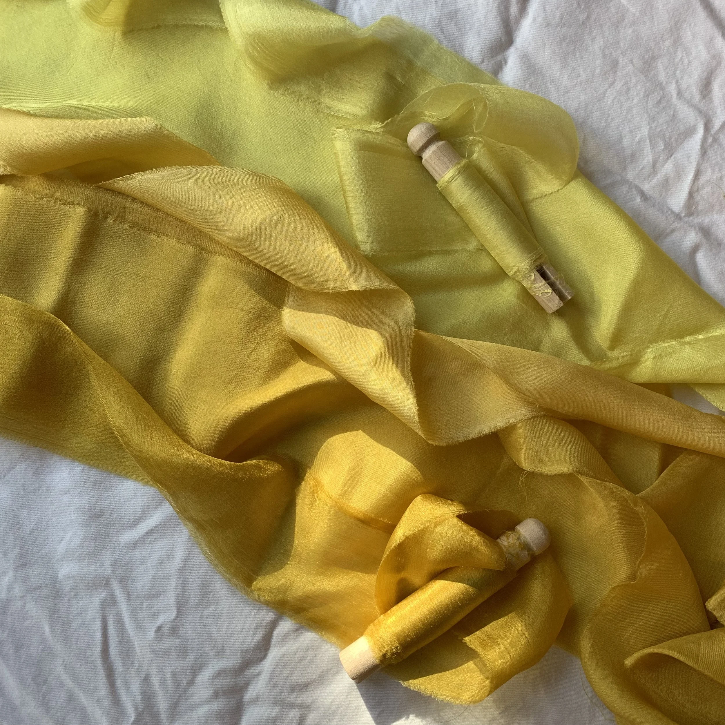 Yellow silk ribbon with wooden spindle and thread on crumpled white paper background.