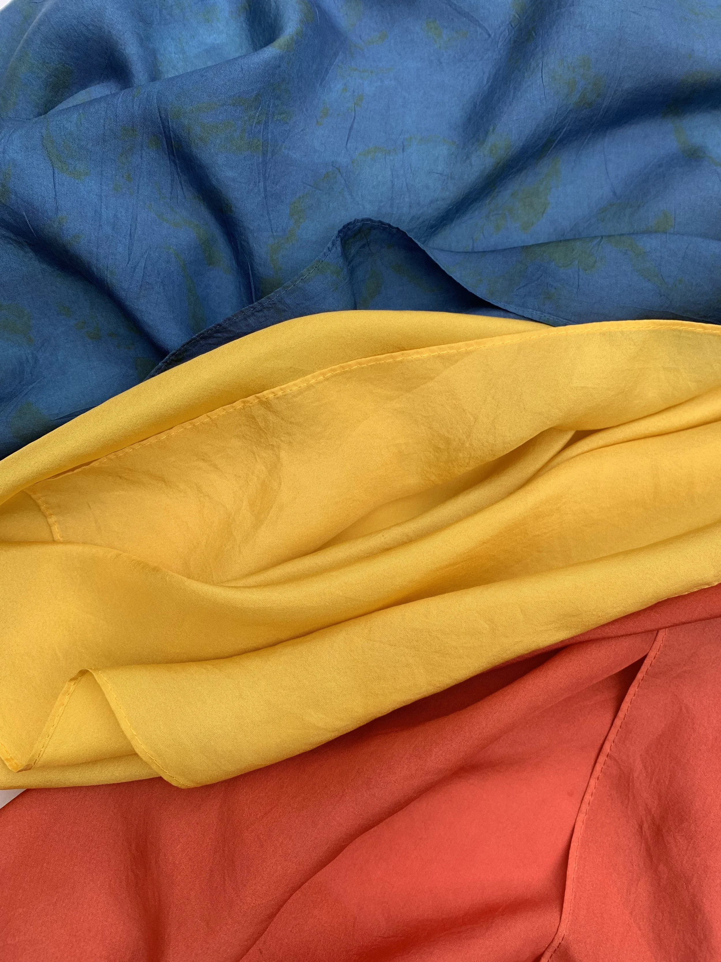 Close-up of naturally dyed silk  scarves in blue, yellow, and red colors layered on top of each other.